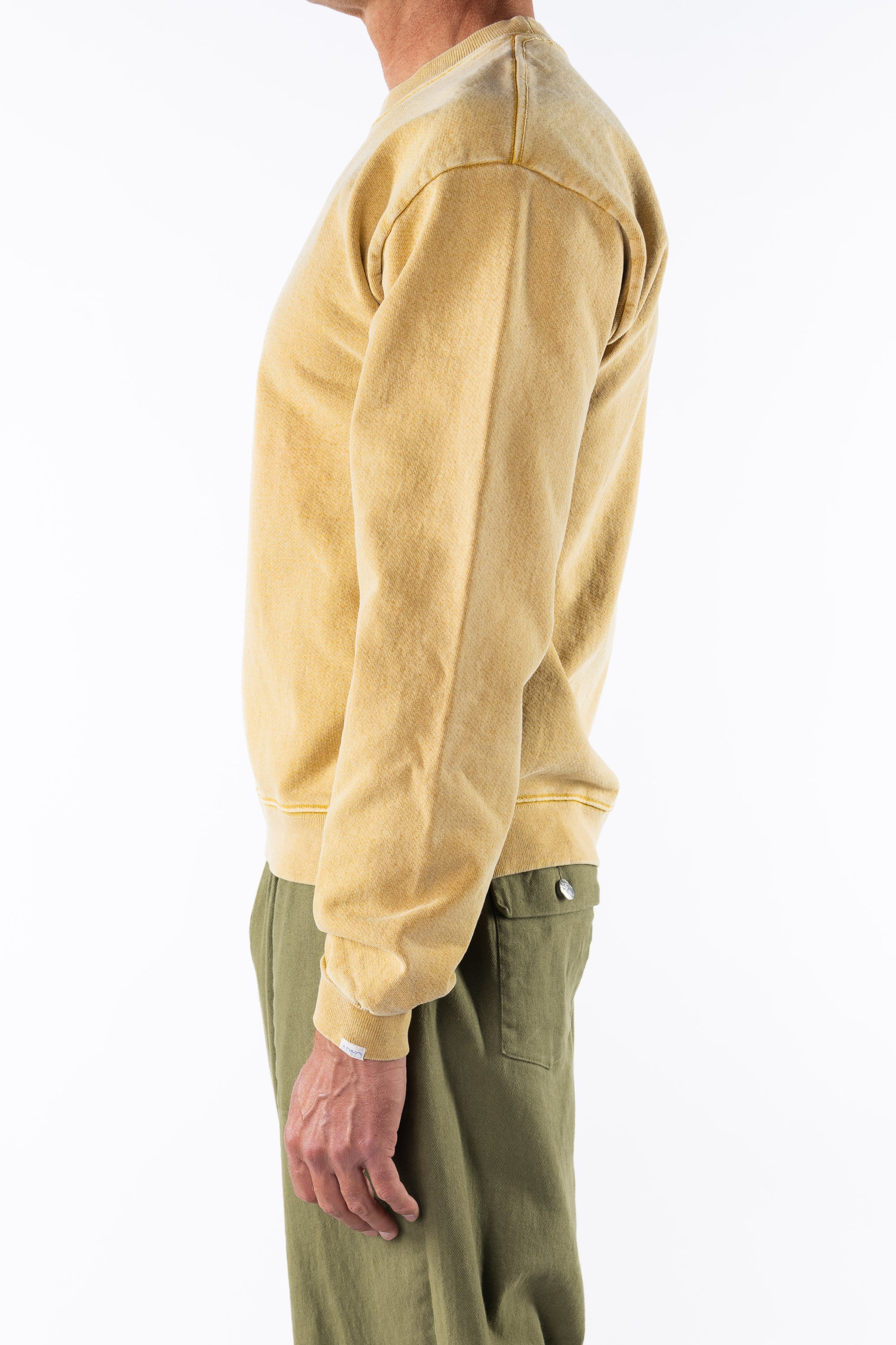 Side view of a person wearing a sunrise yellow sweatshirt and army green day pants on a white background