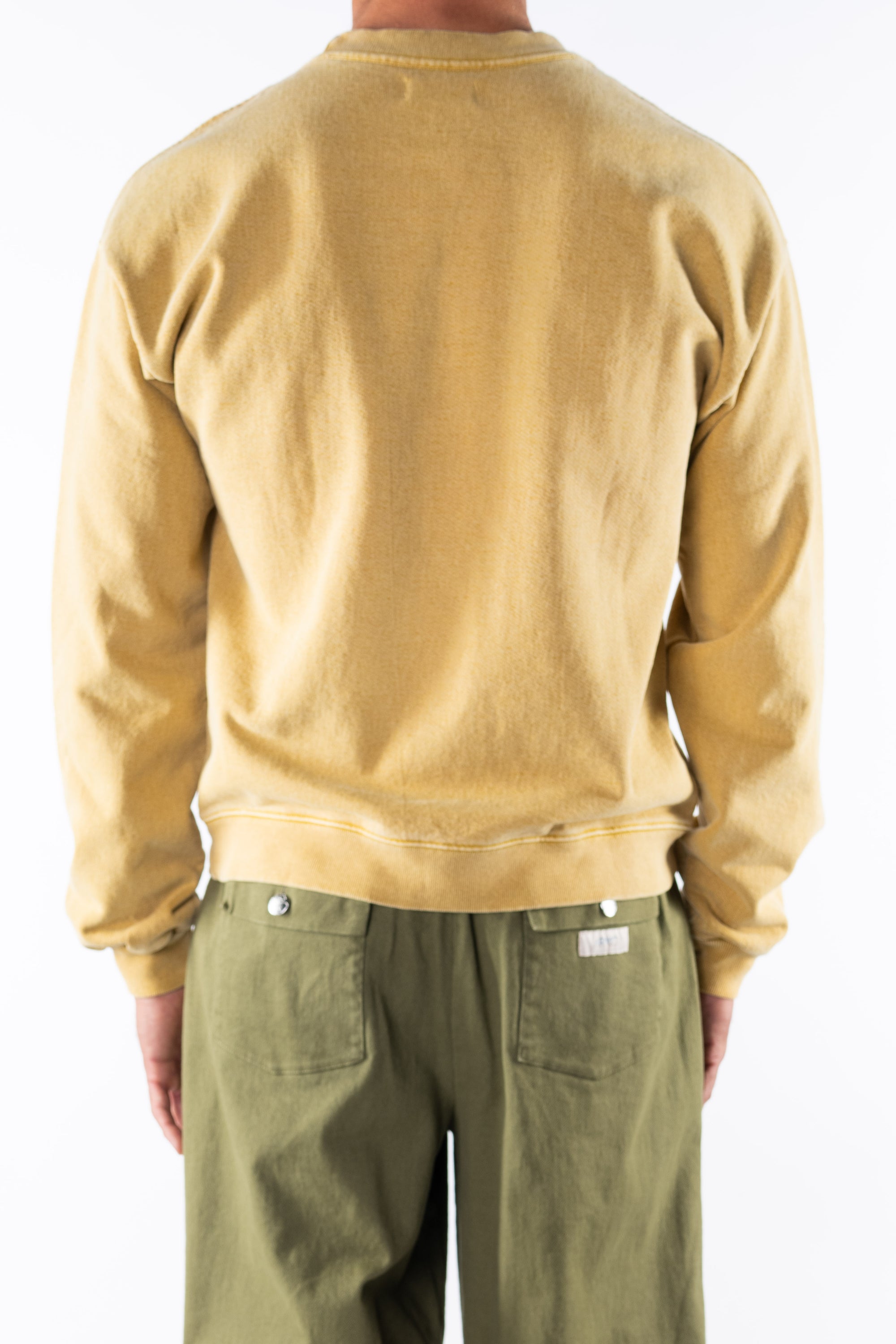 Back view of a person wearing a sunrise yellow sweatshirt and army green day pants on a white background
