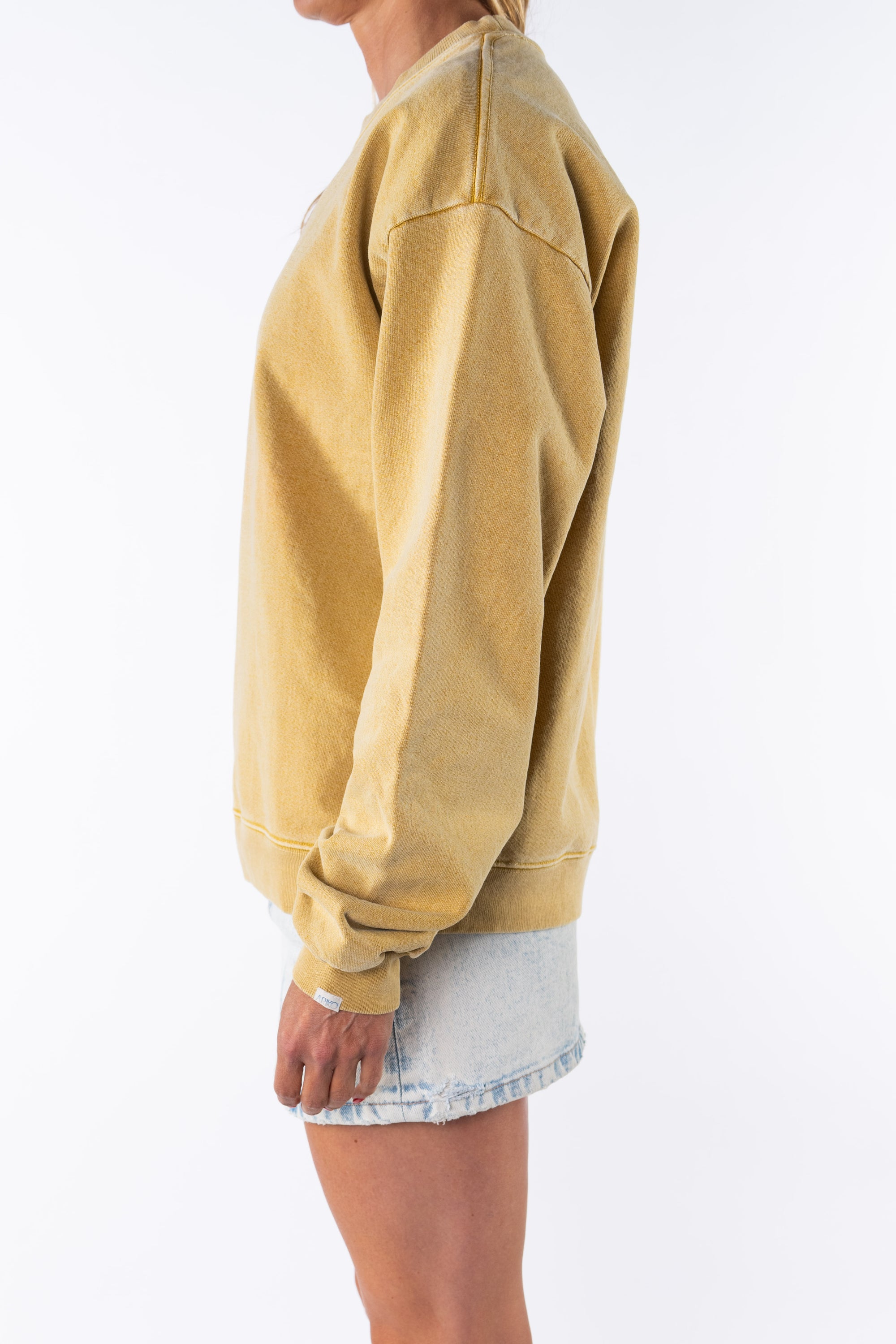 Side view of a woman wearing a yellow oversized sweatshirt and a denim mini skirt on a white background