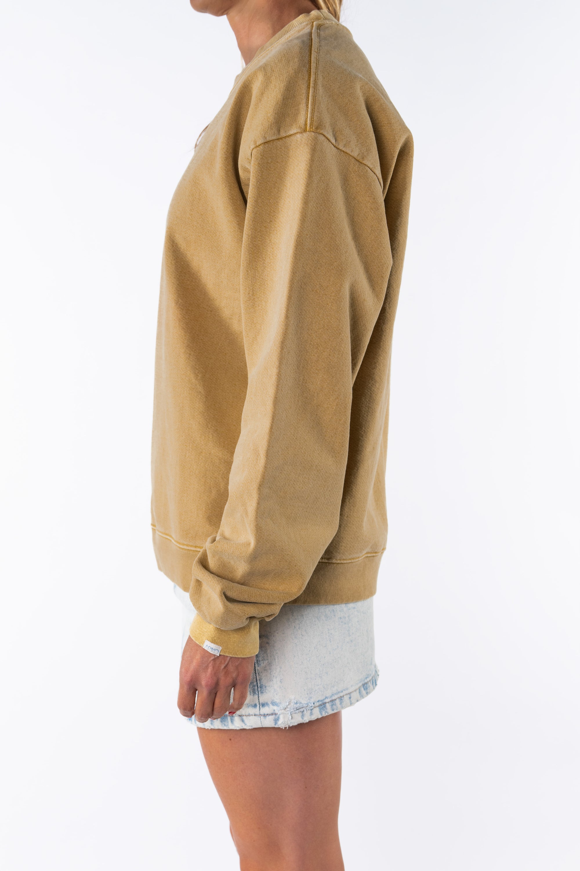 Side view of a woman wearing a sunrise yellow sweatshirt and denim mini skirt on a white background
