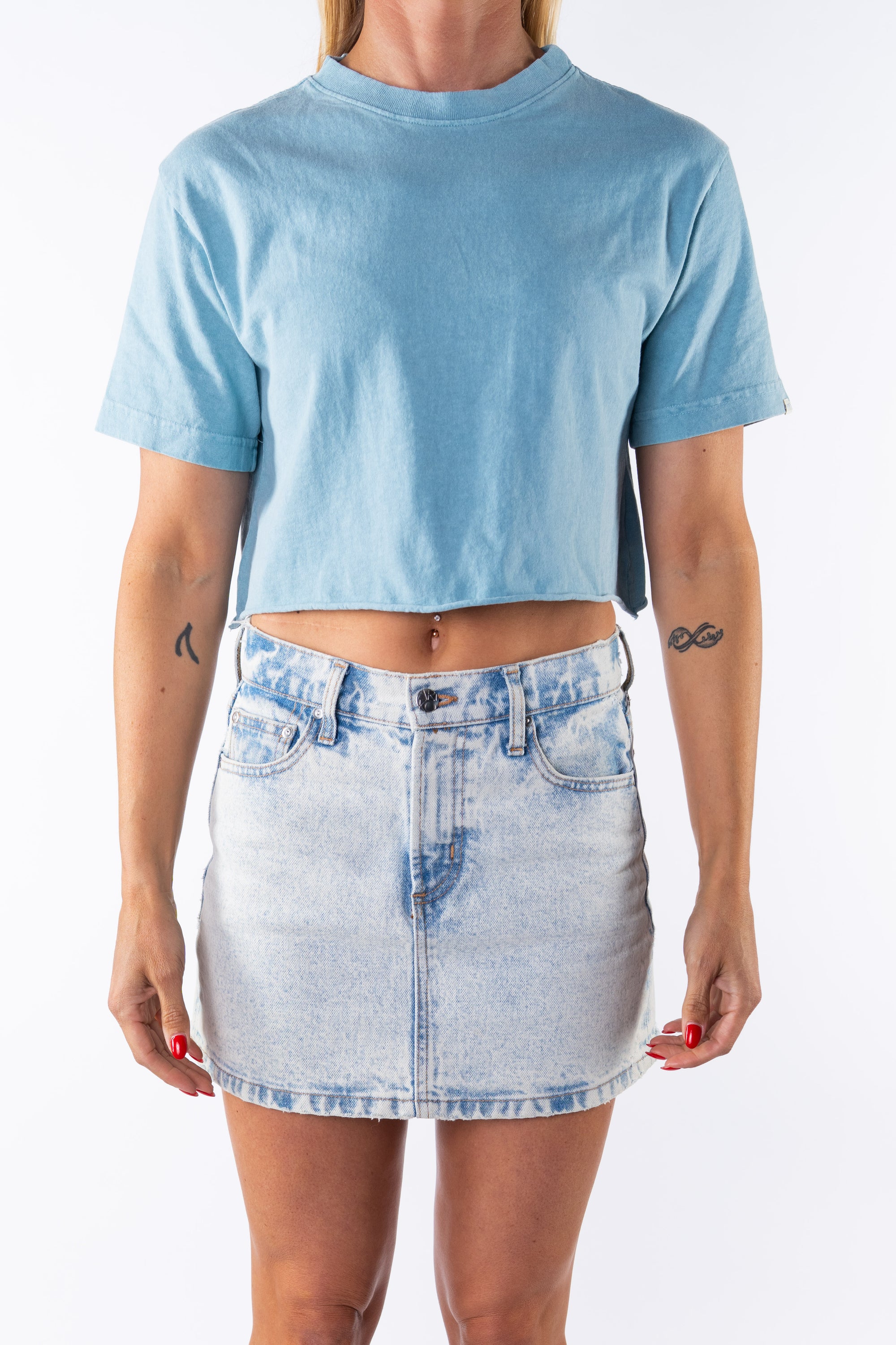 Woman wearing a light blue beach crop t-shirt and denim mini skirt on a white background