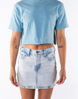 Woman wearing a light blue beach crop t-shirt and denim mini skirt on a white background