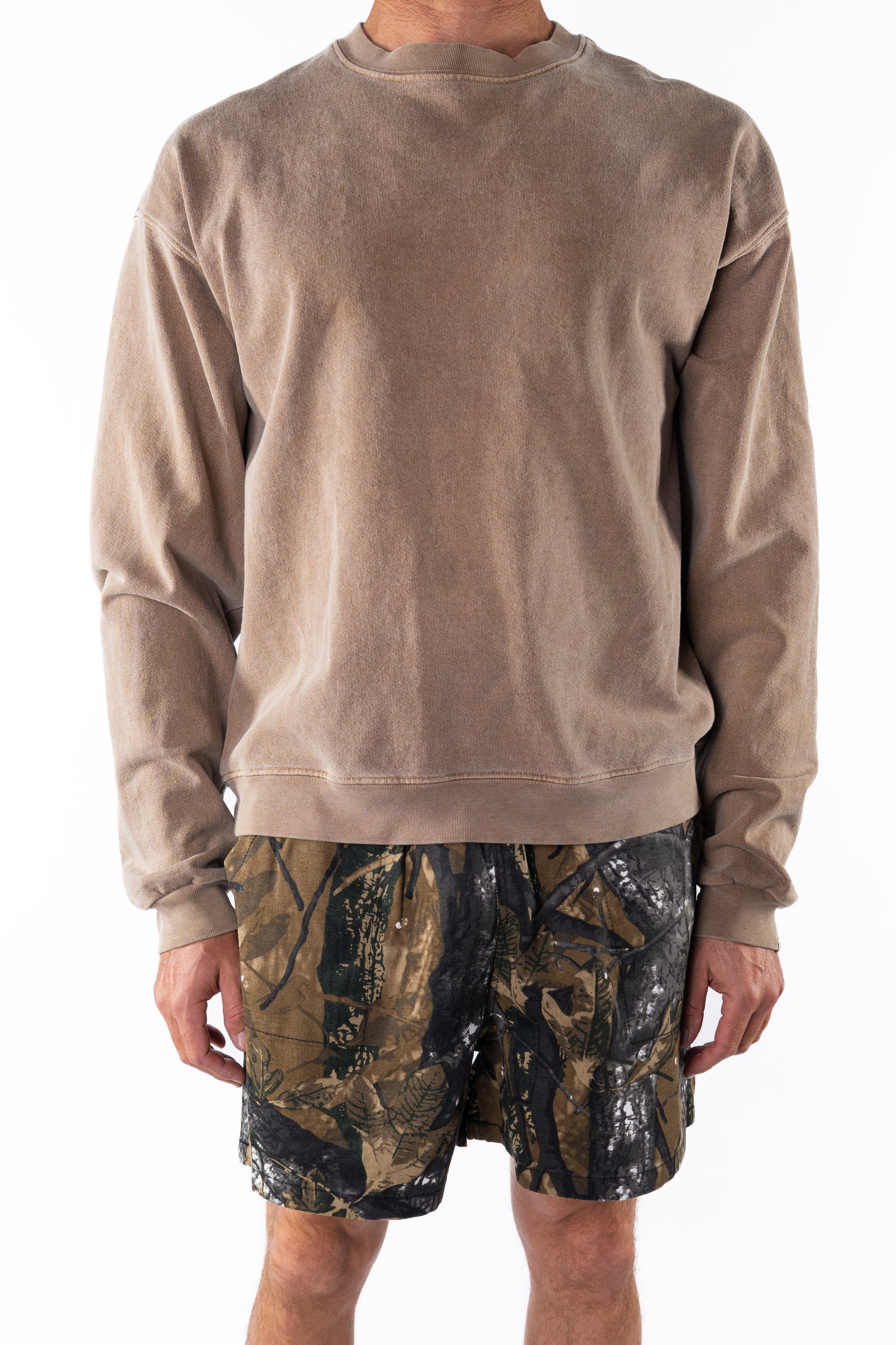 Person wearing a brown sweatshirt and real tree camouflage day shorts on a white background 