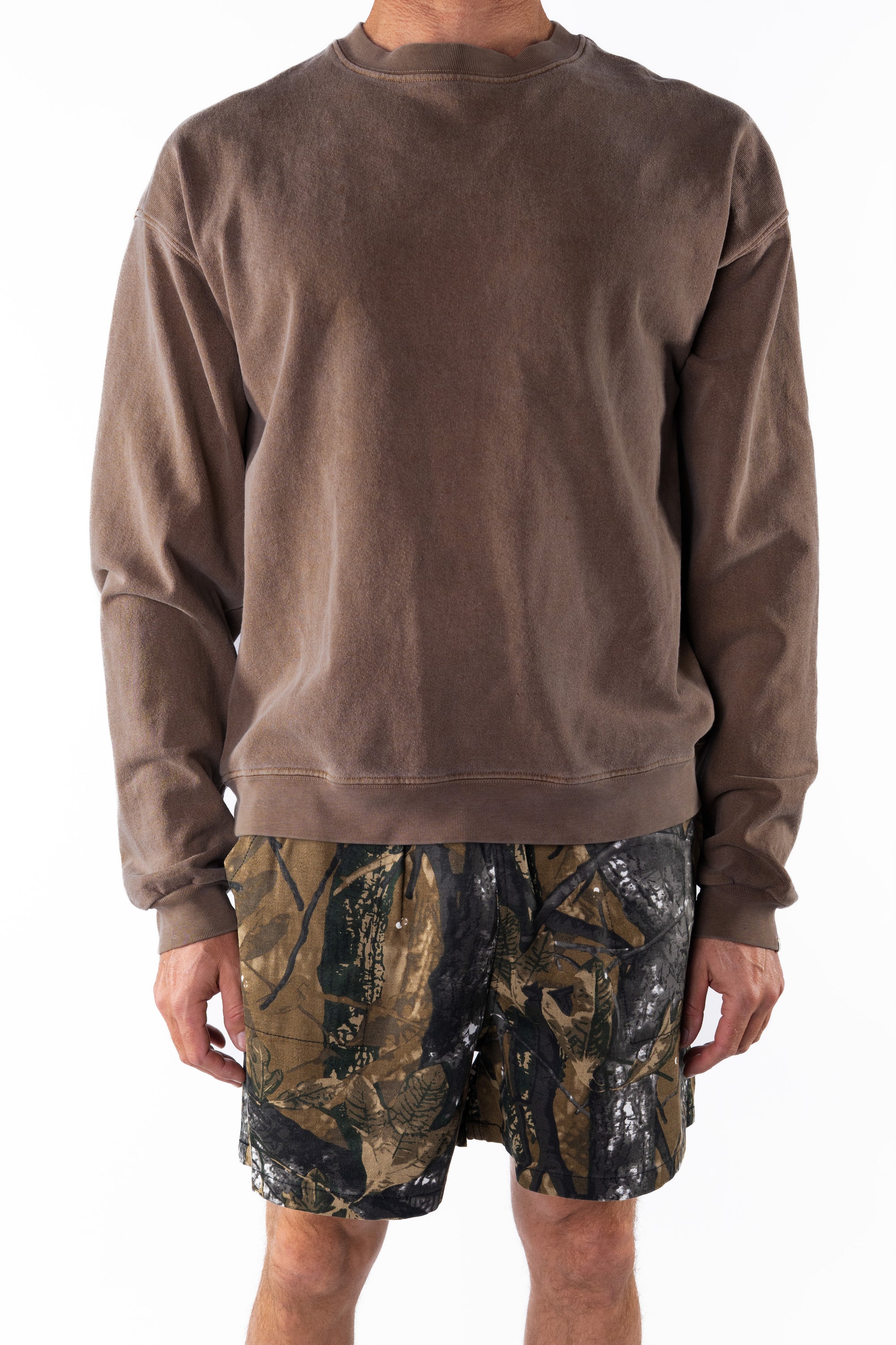 Back view of a person wearing a brown sweatshirt and real tree camouflage day shorts on a white background