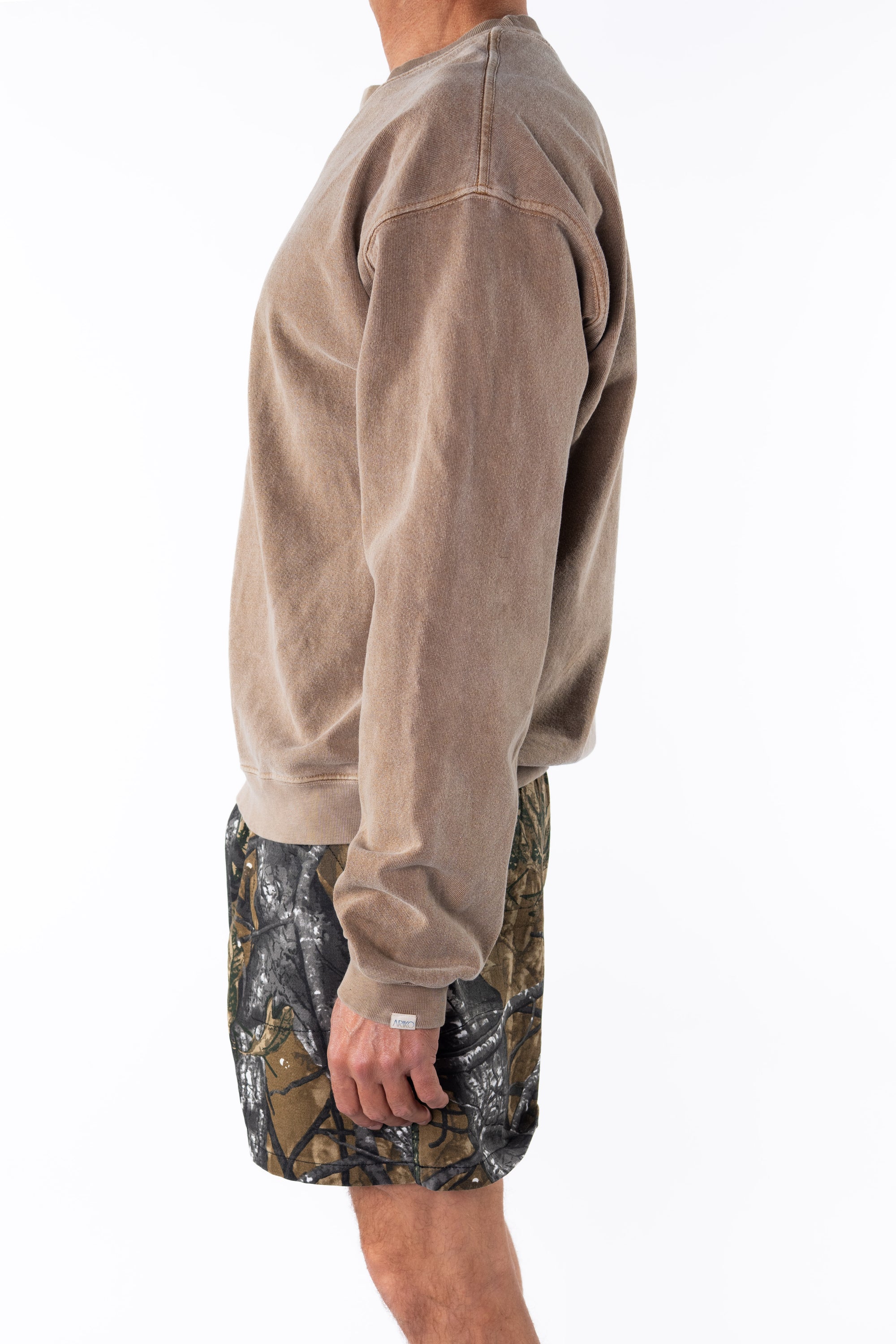 Side view of a person wearing a brown sweatshirt and real tree camouflage day shorts on a white background 