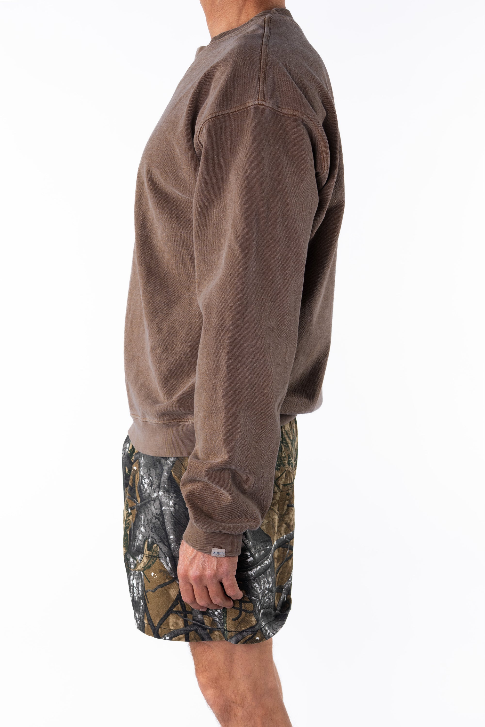 Side view of a person wearing a brown sweatshirt and real tree camouflage day shorts on a white background