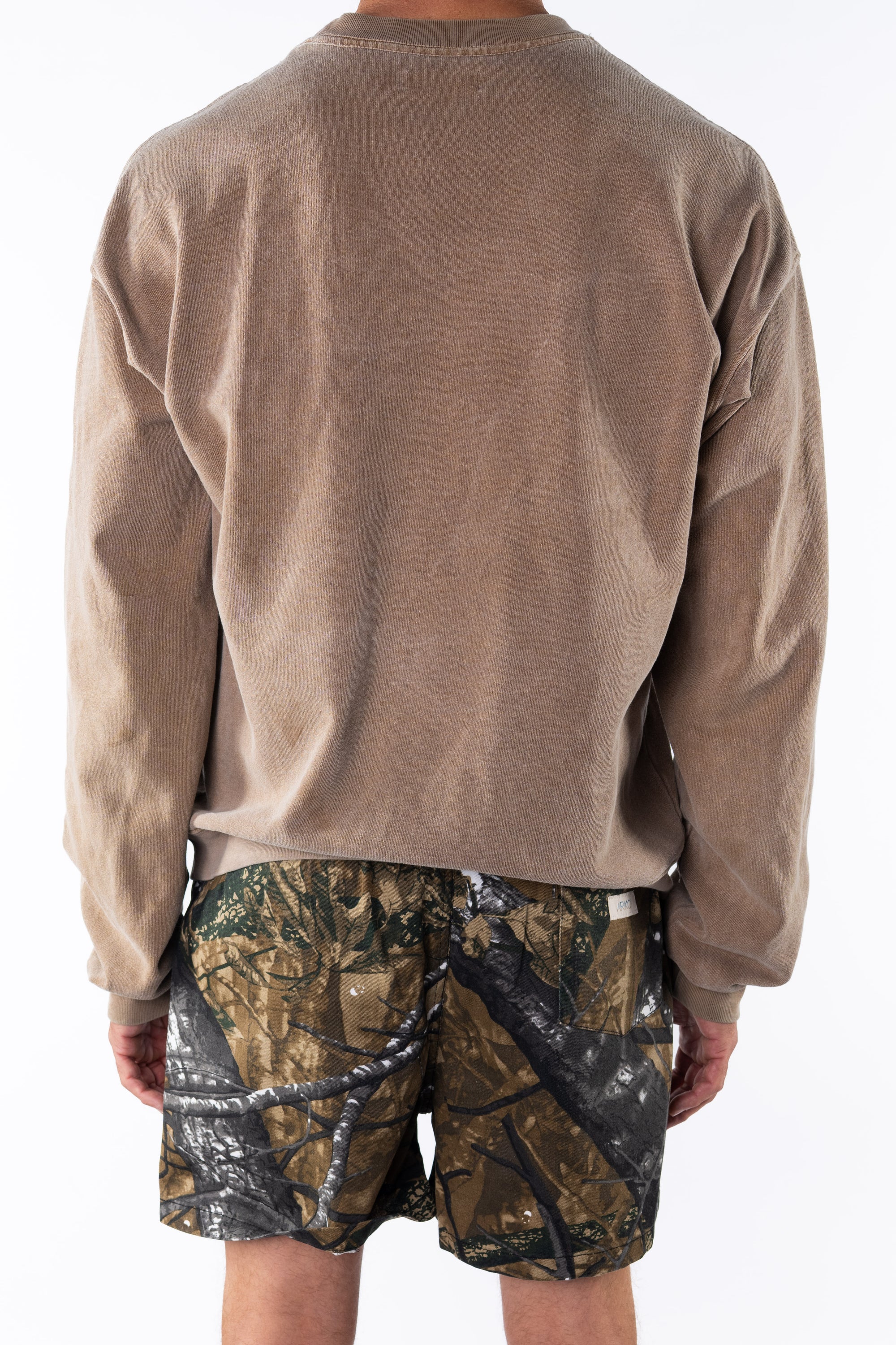 Back view of a person wearing a brown sweatshirt and real tree camouflage day shorts on a white background