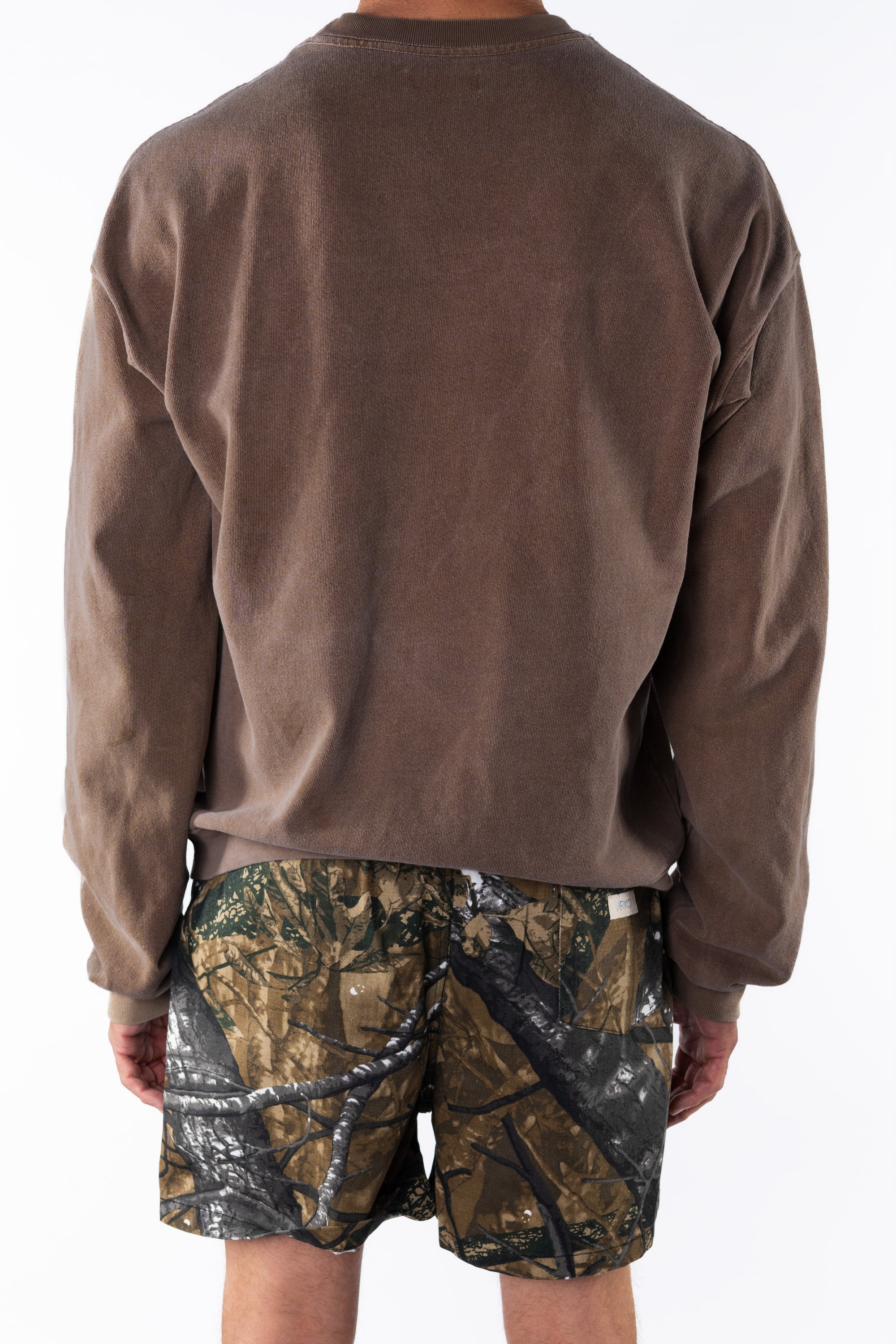Back view of a person wearing a brown sweatshirt and real tree camouflage day shorts on a white background