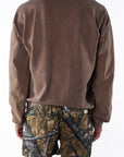 Back view of a person wearing a brown sweatshirt and real tree camouflage day shorts on a white background