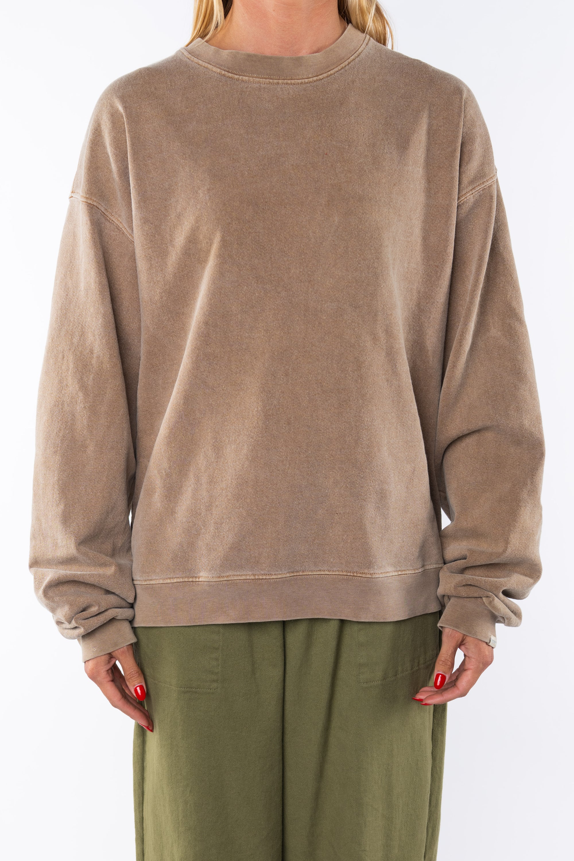 Woman wearing a brown post surf crw sweatshirt and army green day pants on a white background