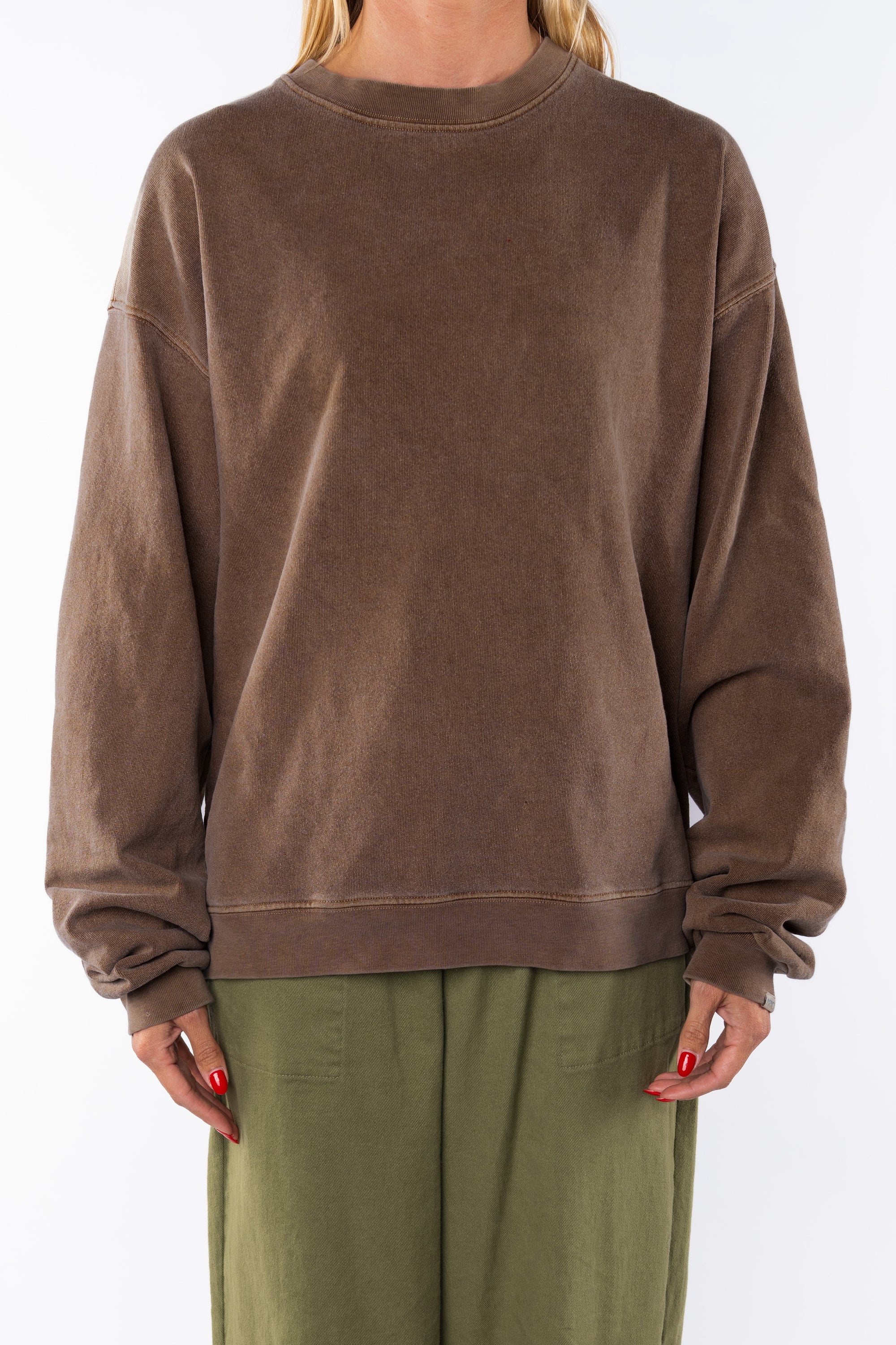 Woman wearing a brown sweatshirt and army green day pants on a white background