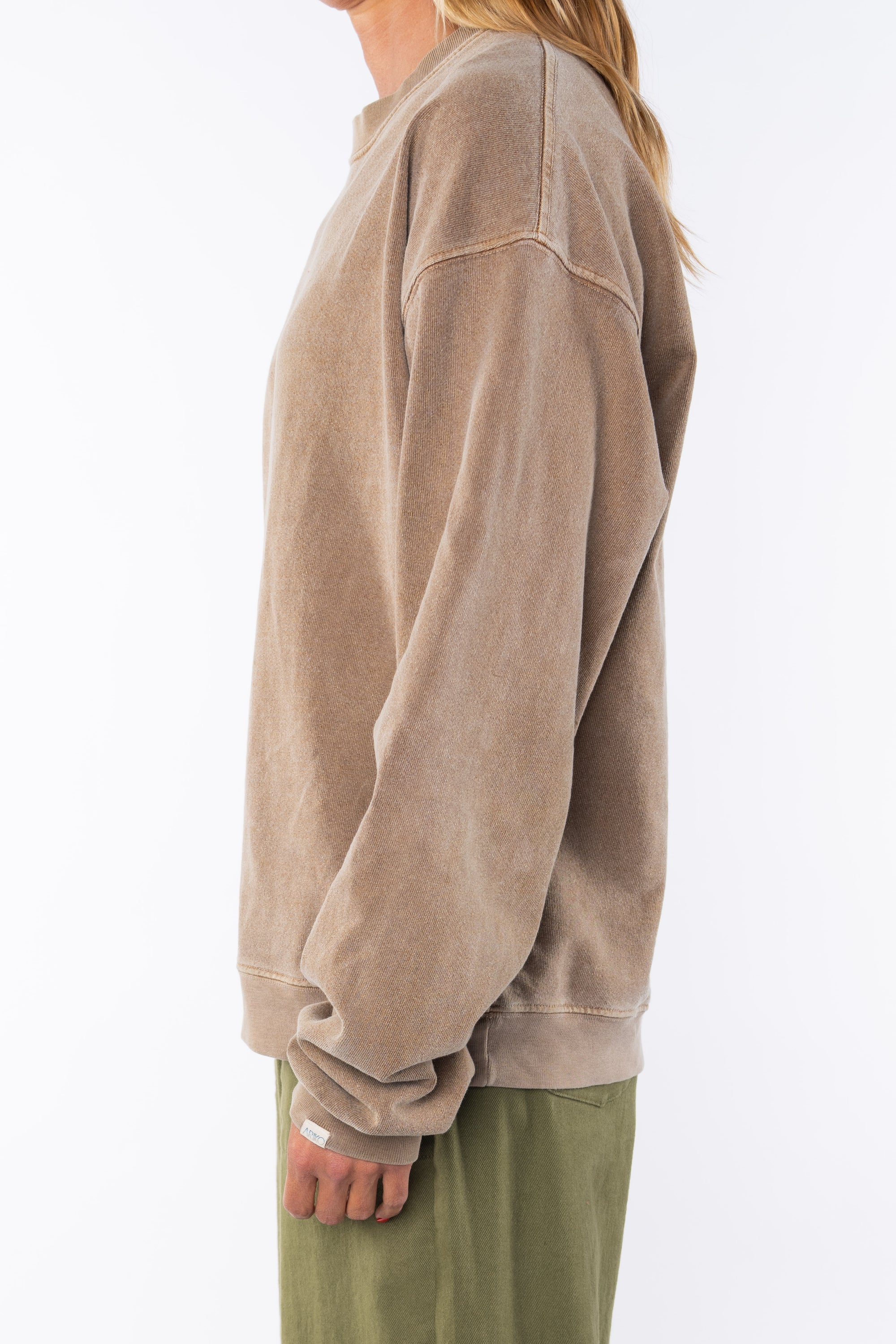 Side view of a woman wearing a brown sweatshirt and army green day pants on a white background