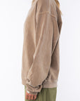 Side view of a woman wearing a brown sweatshirt and army green day pants on a white background