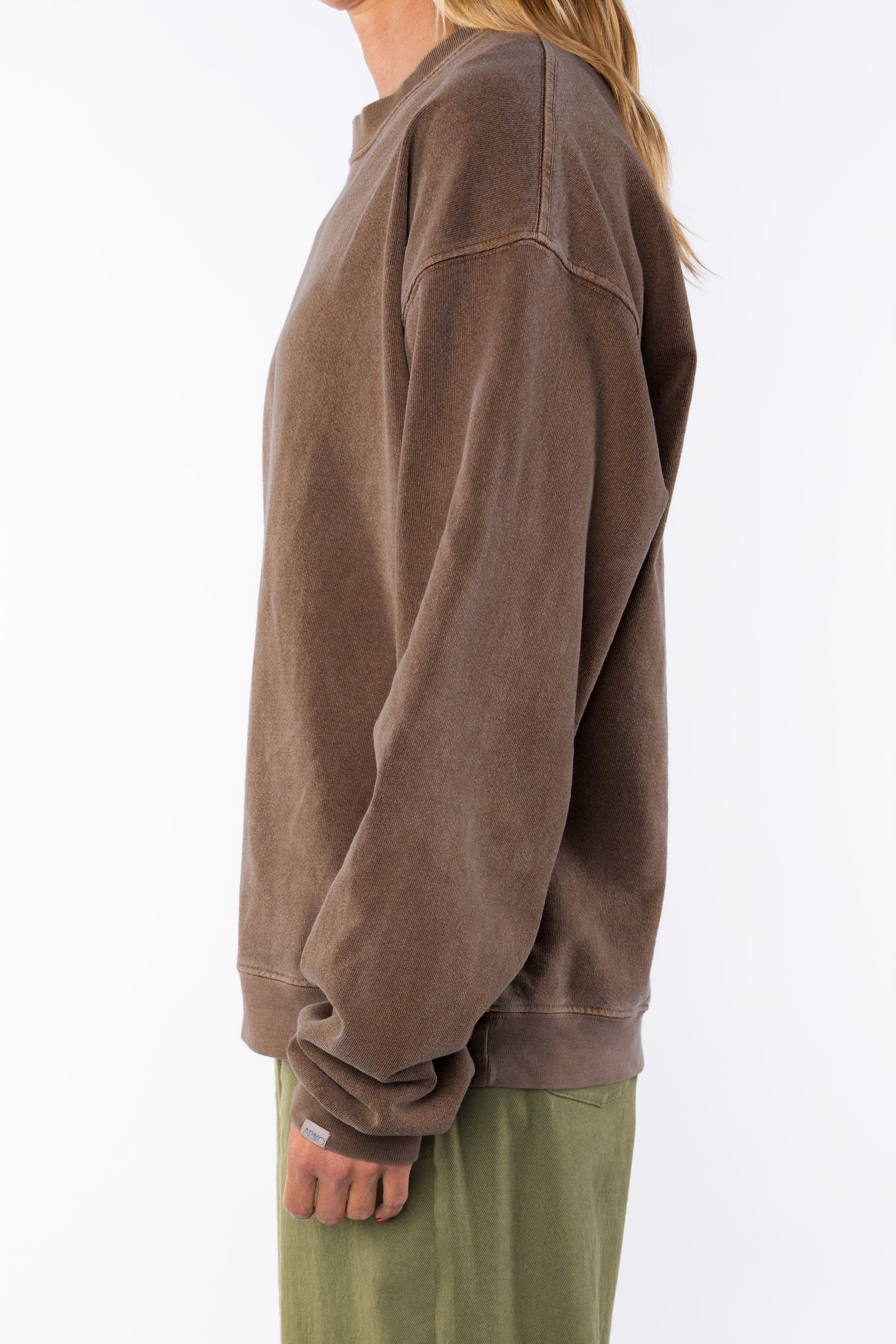 Side view of a woman wearing a brown oversized sweatshirt on a white background with army green day pants