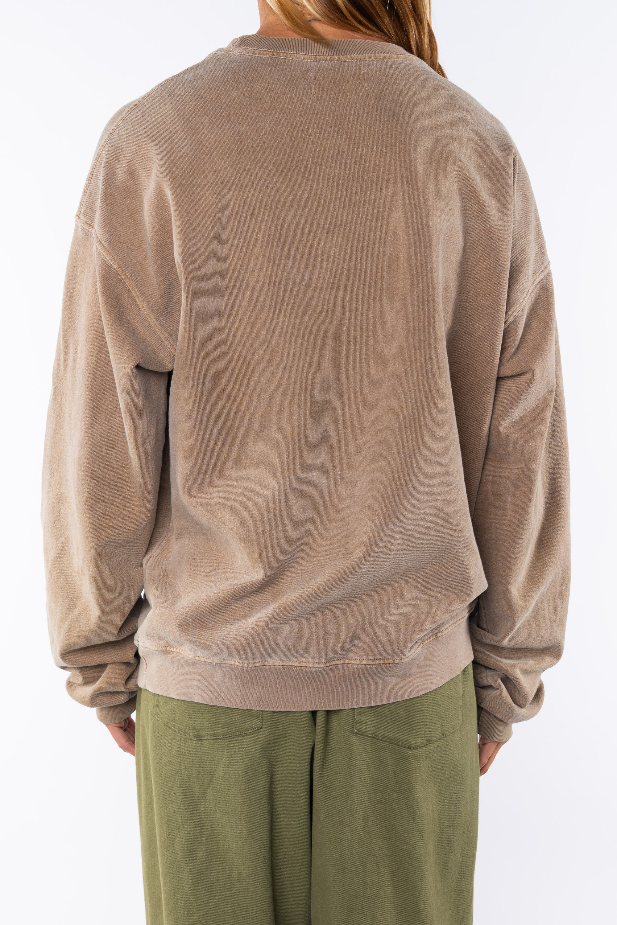 Back view of a woman wearing a brown post surf crew sweatshirt and army green day pants on a white background