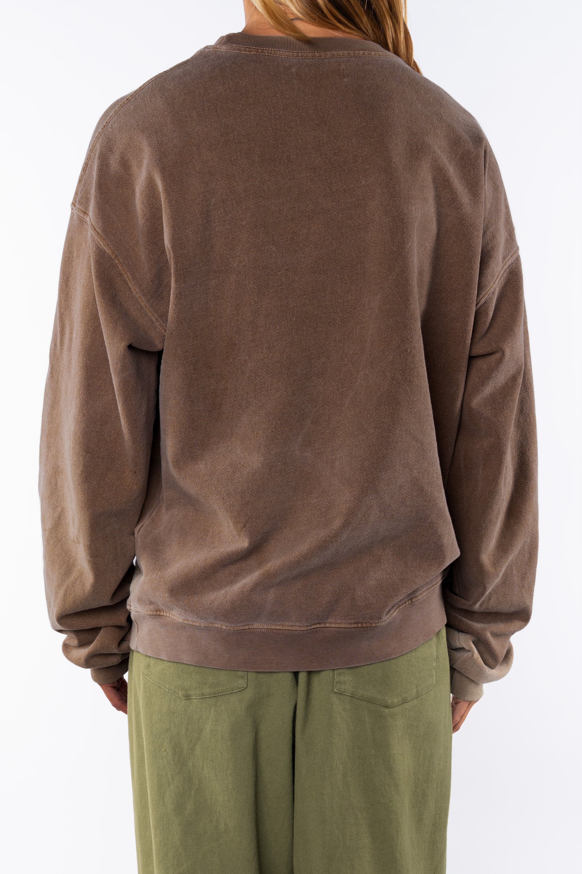 Back view of a woman wearing a brown sweatshirt and army green day pants on a white background