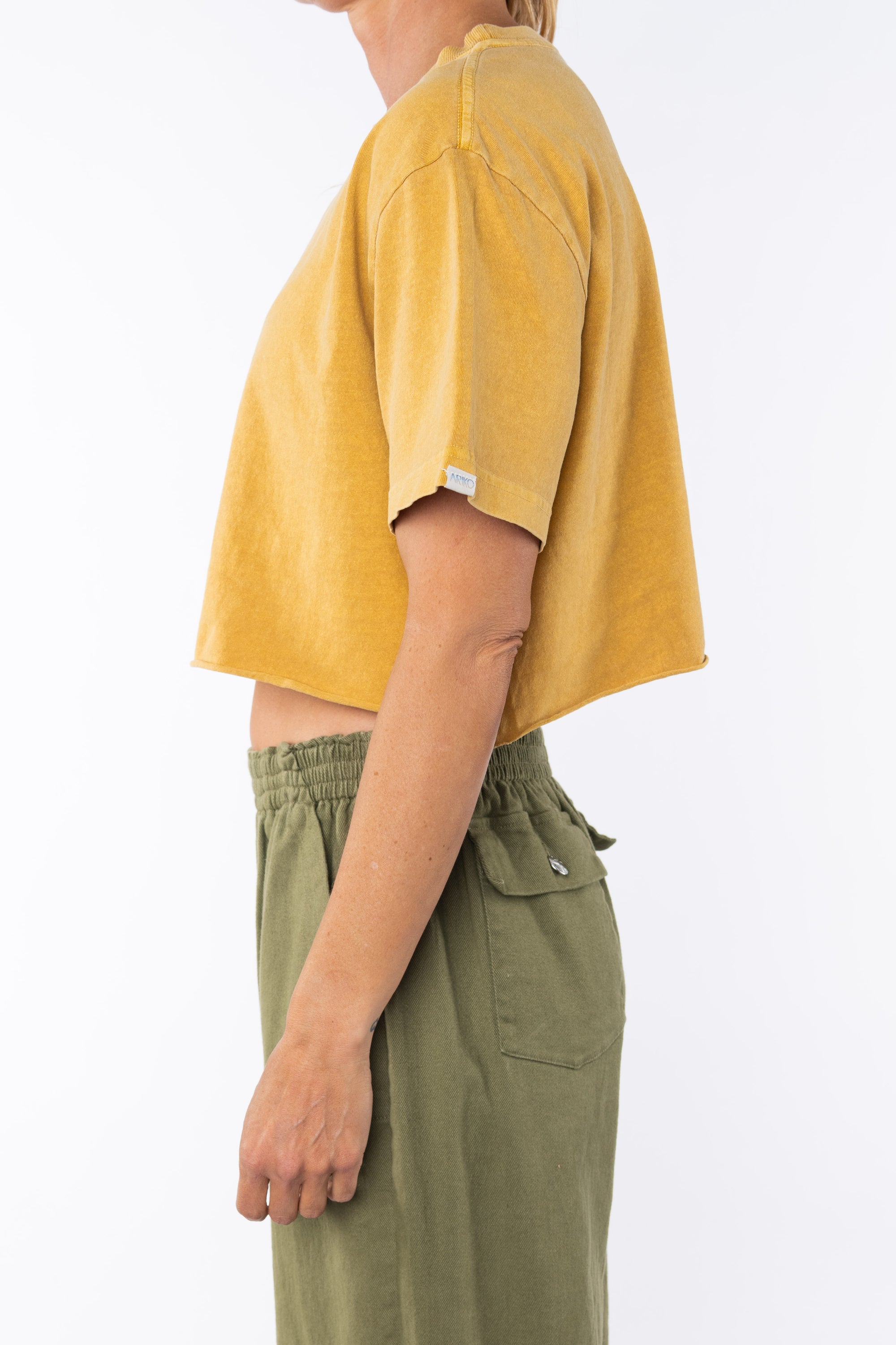 Side view of a woman wearing beach crop t-shirt in sunrise yellow with army green day pants