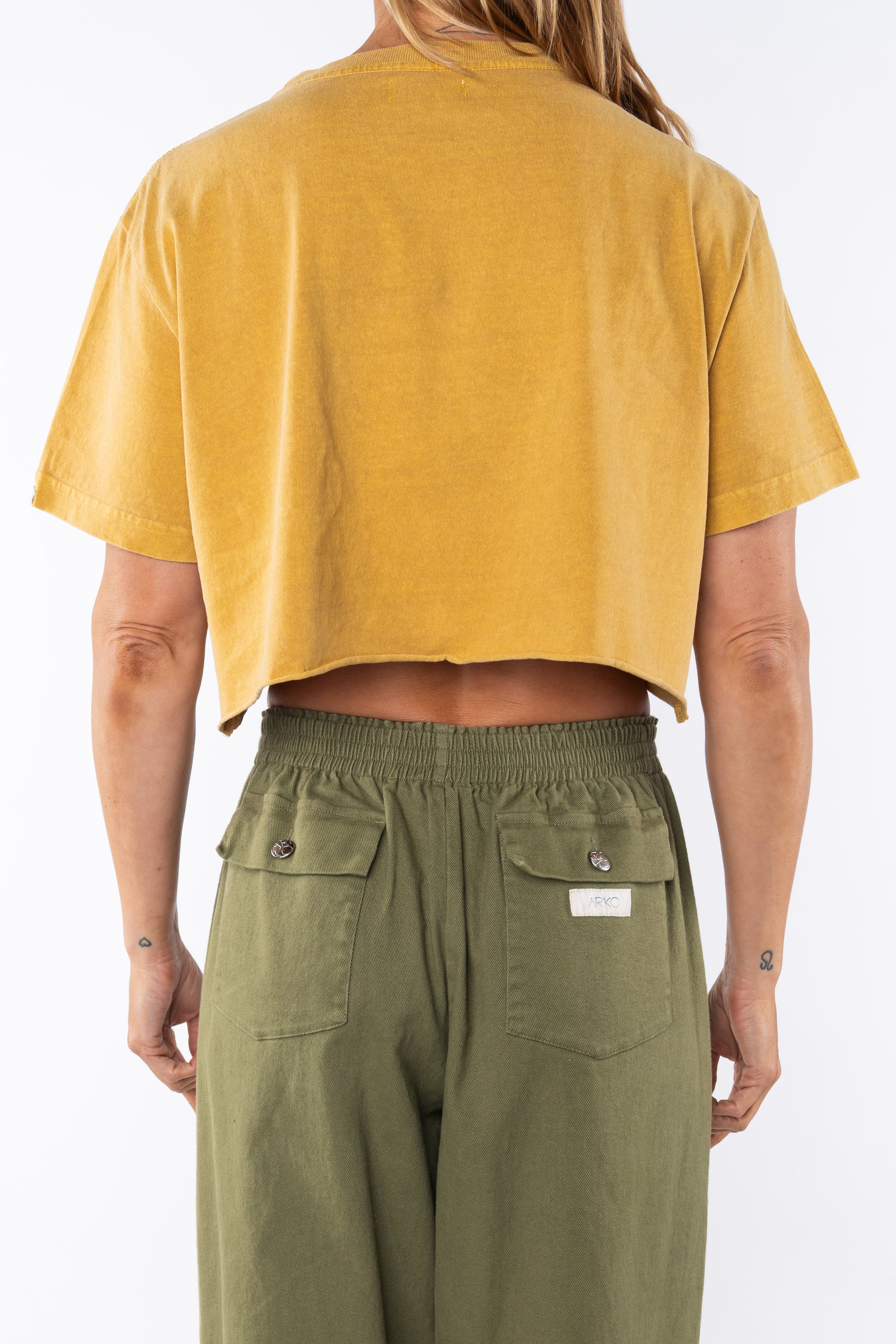 Woman wearing a sunrise yellow crop t-shirt and army green day pants on a white background