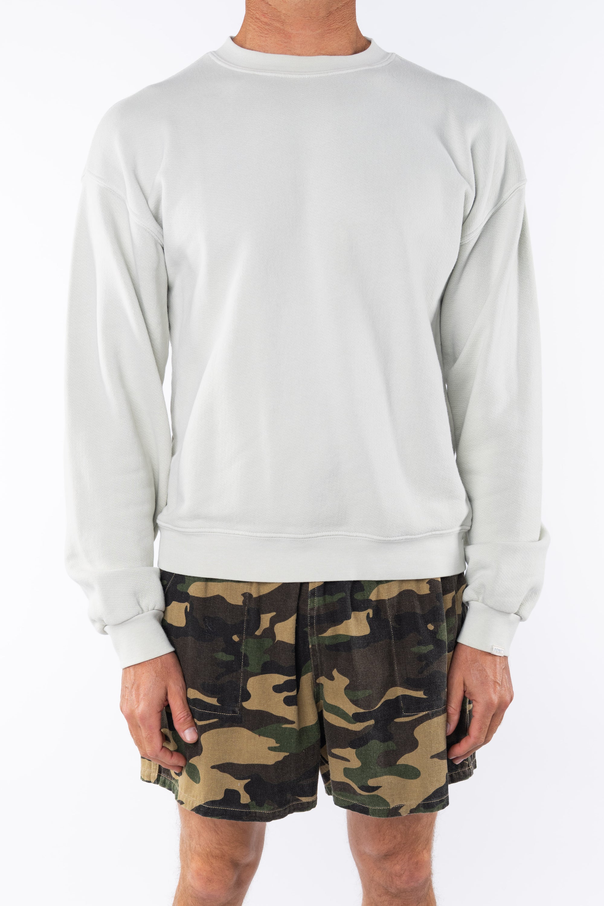 person wearing a beige sweatshirt and camouflage shorts on a white background
