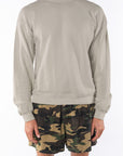 Person wearing a beige sweatshirt and camouflage day shorts on a white background