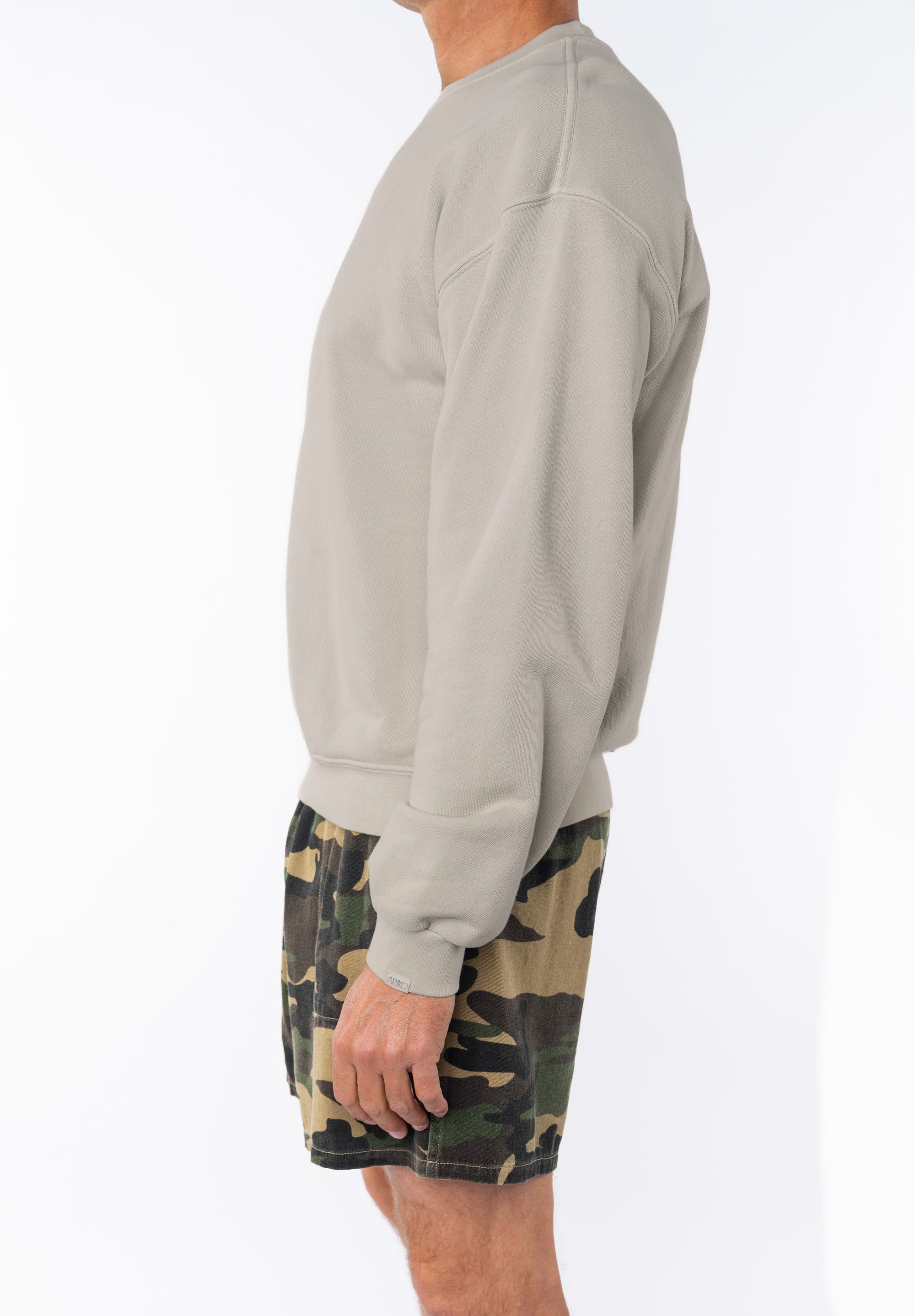 Side view of a person wearing a beige sweatshirt and camouflage shorts on a white background