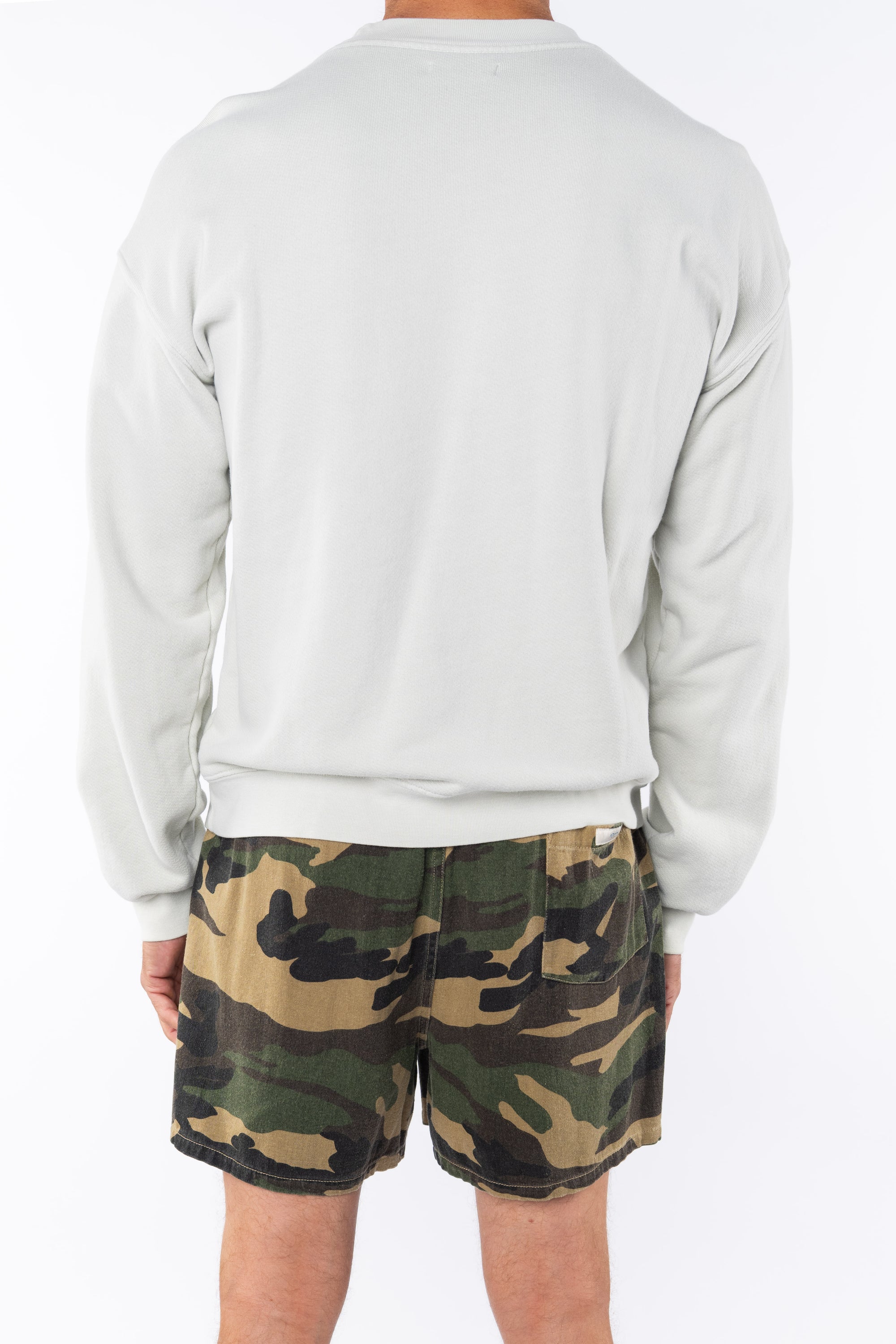 Back view of a person wearing a beige sweatshirt and camouflage shorts on a white background