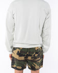 Back view of a person wearing a beige sweatshirt and camouflage shorts on a white background