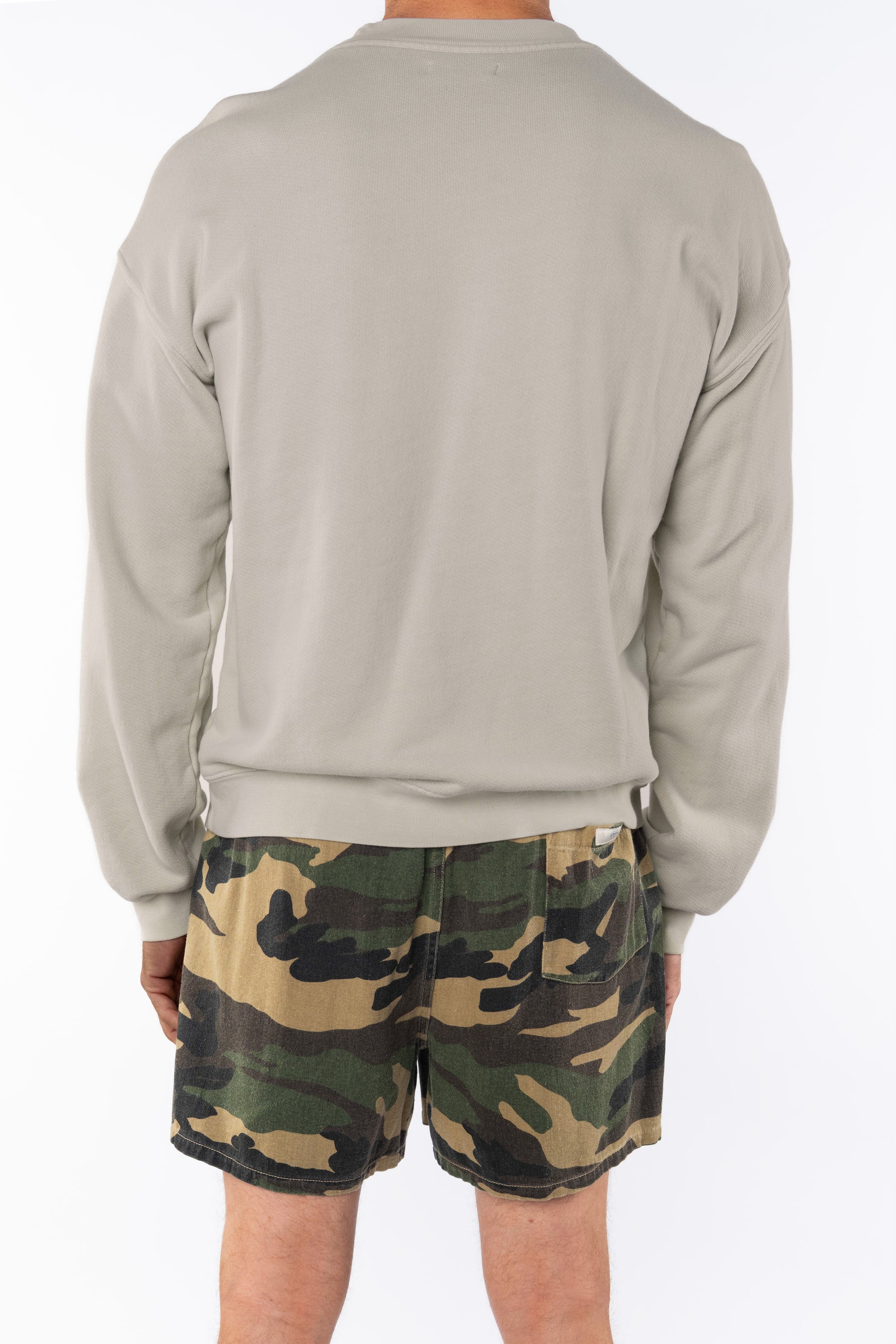 Back view of a person wearing a beige sweatshirt and camouflage day shorts on a white background