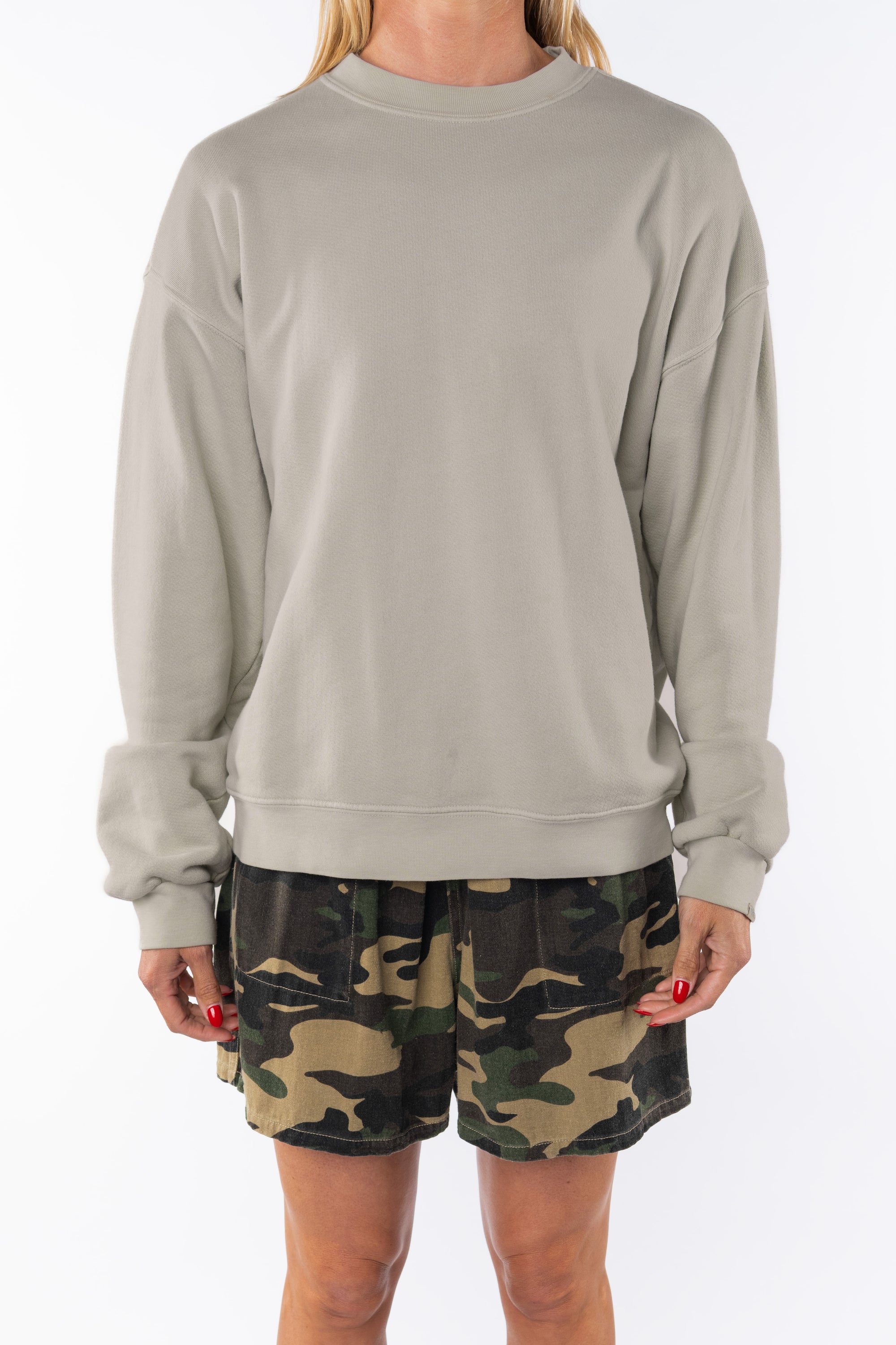 Woman wearing a beige sweatshirt and camouflage day shorts on a white background