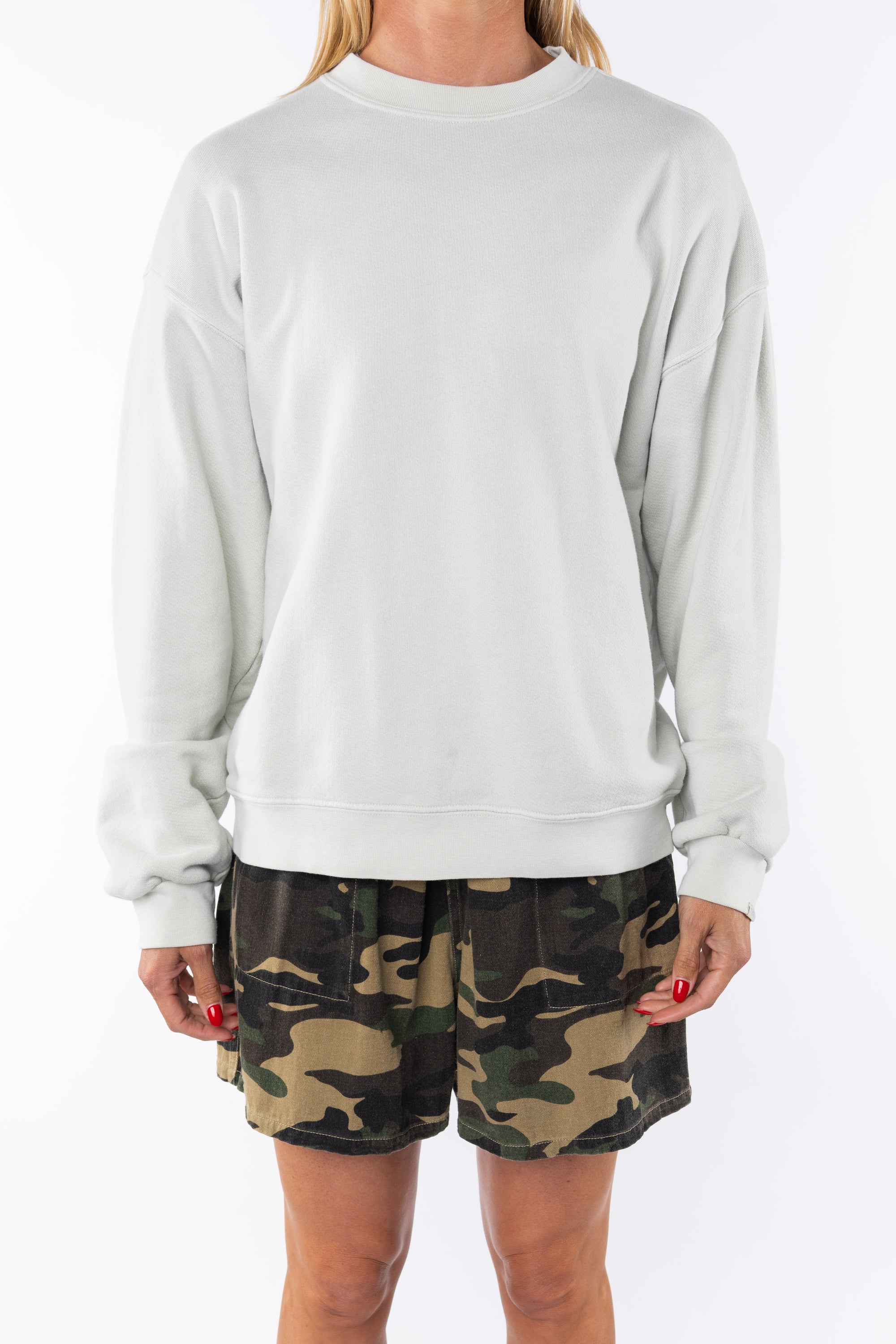 Woman wearing a beige sweatshirt and camouflage day shorts on a white background