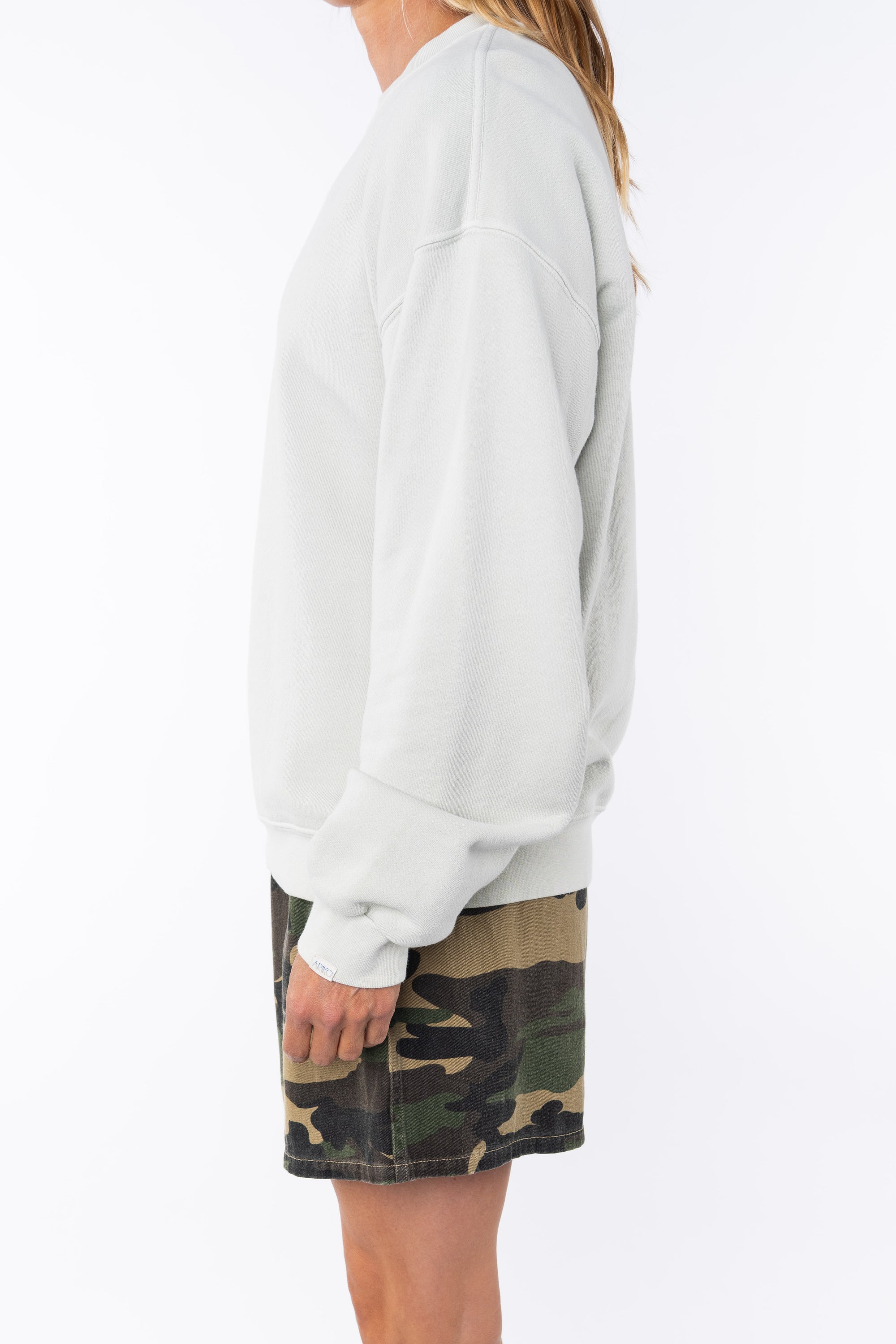 side view of a woman wearing a beige sweatshirt and camouflage day shorts on a white background