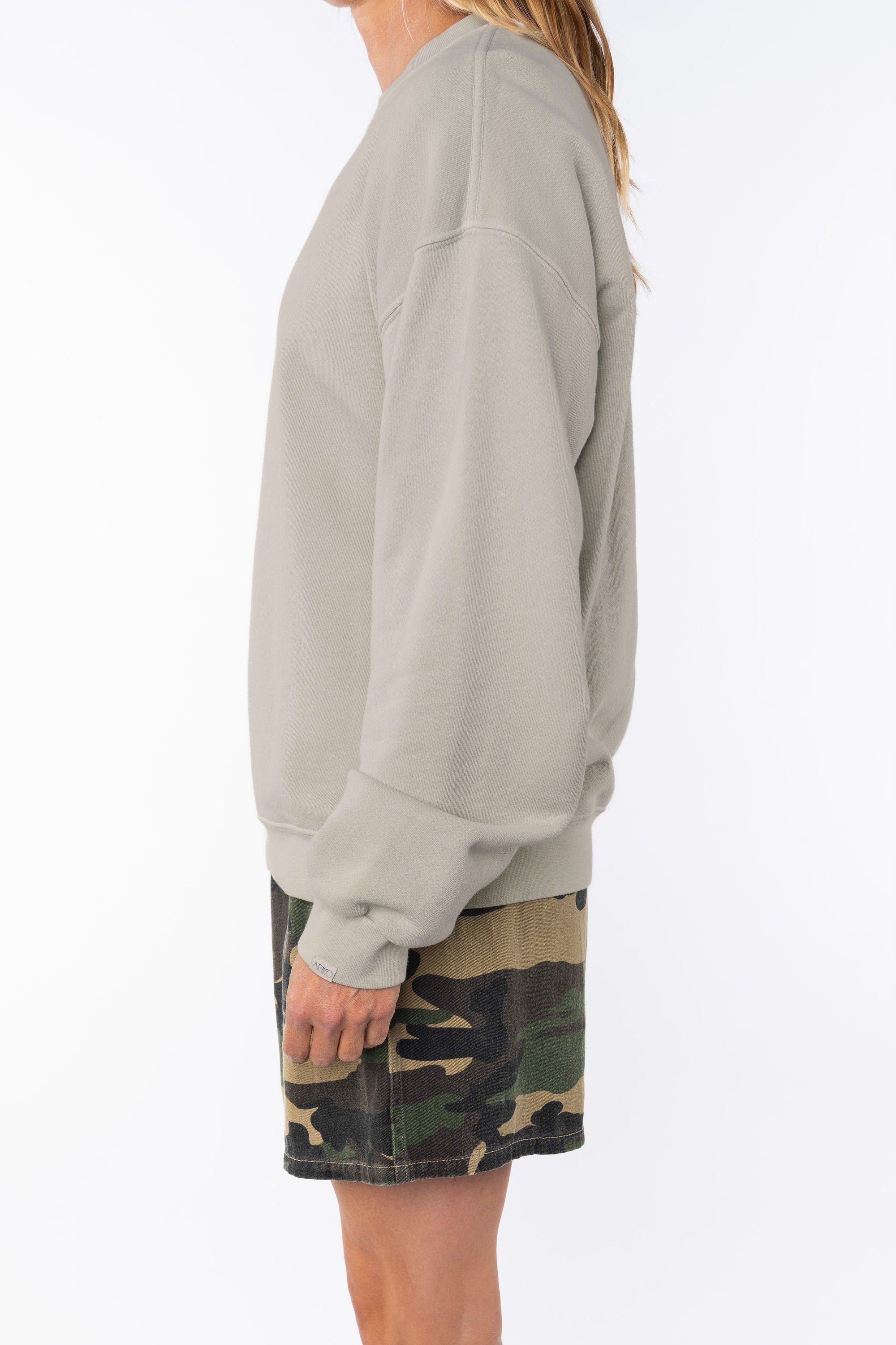Side view of a woman wearing a beige sweatshirt and camouflage day shorts on a white background