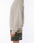 Side view of a woman wearing a beige sweatshirt and camouflage day shorts on a white background