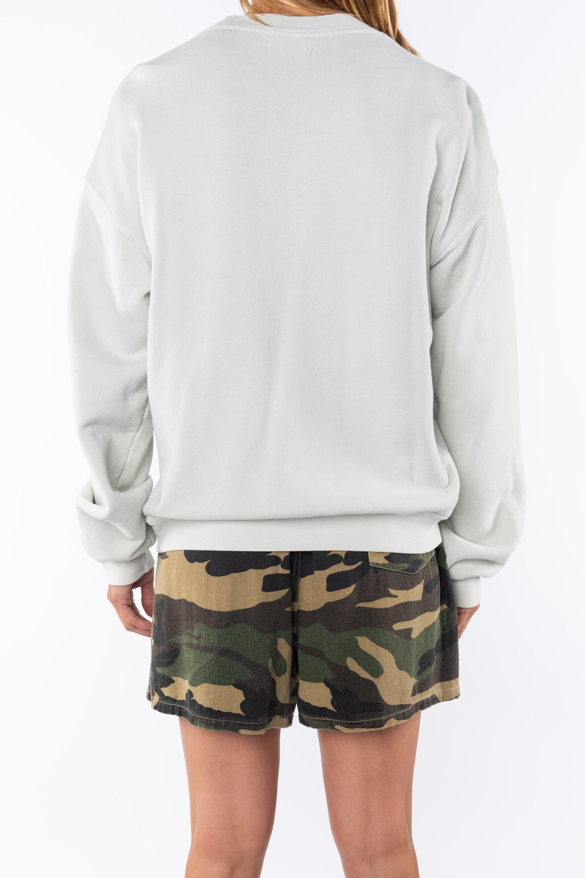 Back view of a woman wearing a beige sweatshirt and camouflage day shorts on a white background
