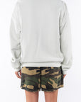 Back view of a woman wearing a beige sweatshirt and camouflage day shorts on a white background