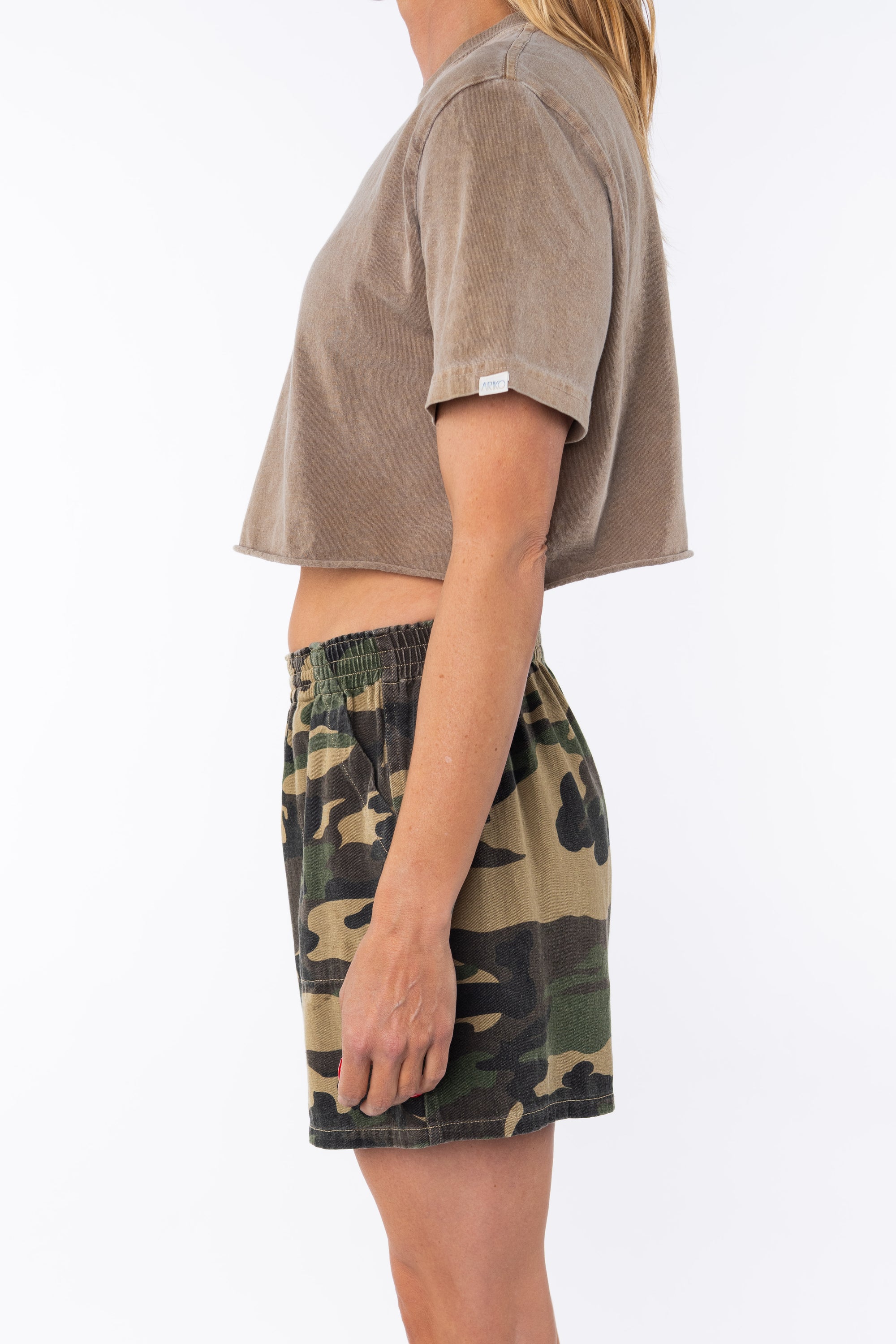 Woman wearing a brown beach crop t-shirt and camouflage day shorts on a white background