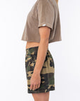 Woman wearing a brown beach crop t-shirt and camouflage day shorts on a white background