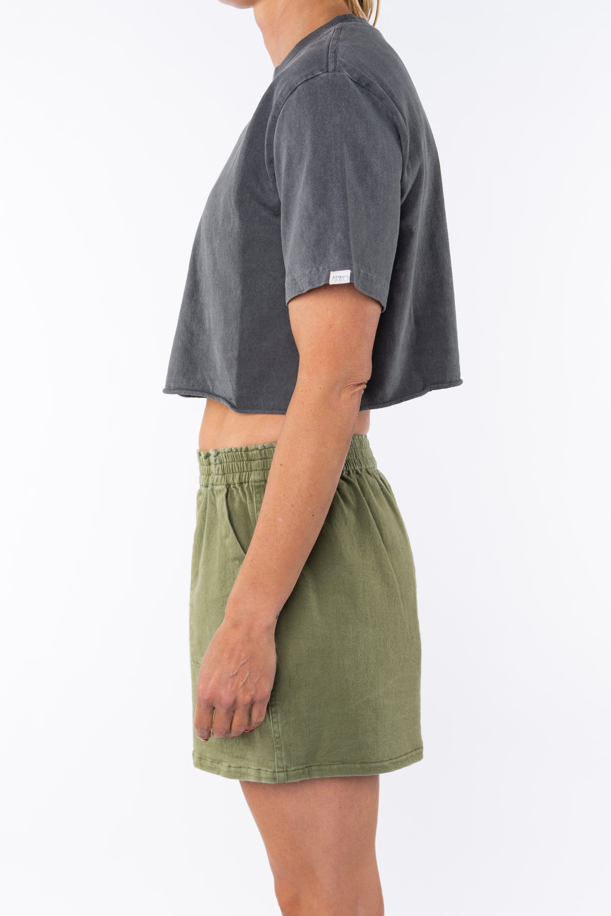 Side view of a woman wearing a sea gray cropped t-shirt and army green day shorts on a white background