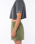 Side view of a woman wearing a sea gray cropped t-shirt and army green day shorts on a white background