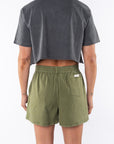 Back shot of a woman wearing a Beach Crop Tee in Sea Gray with Army Green day shorts. 