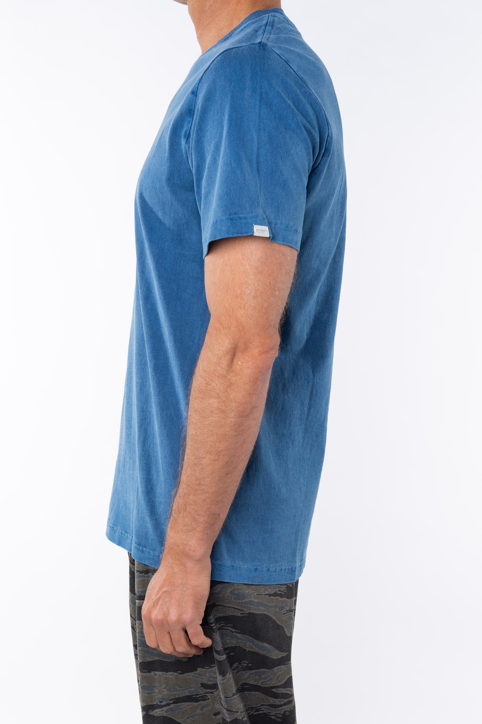 Side view of a man wearing a teal beach t-shirt with ocean tiger camo day pants on a white background 