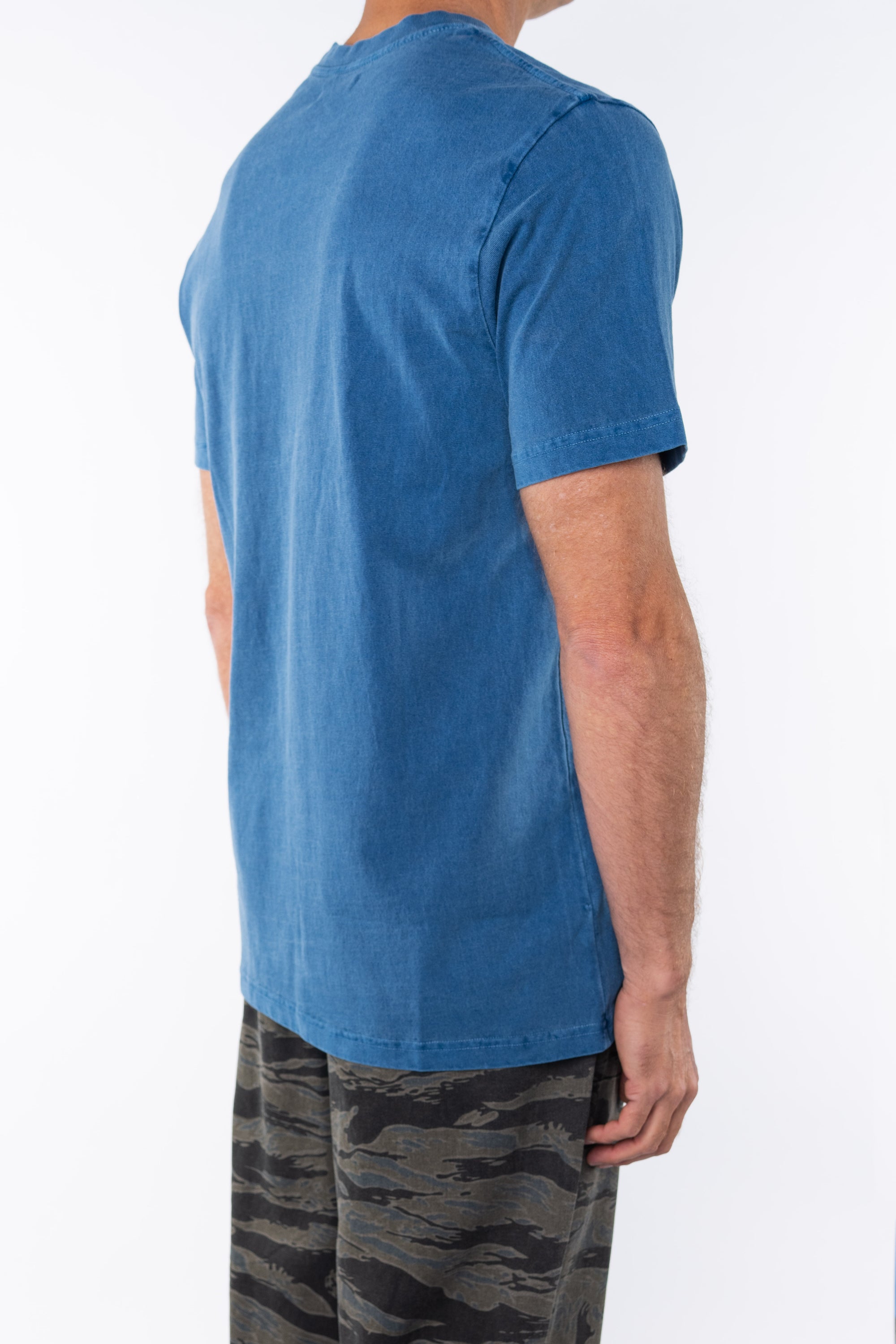 Side back view of a man wearing a teal beach t-shirt with ocean tiger camo day pants on a white background 