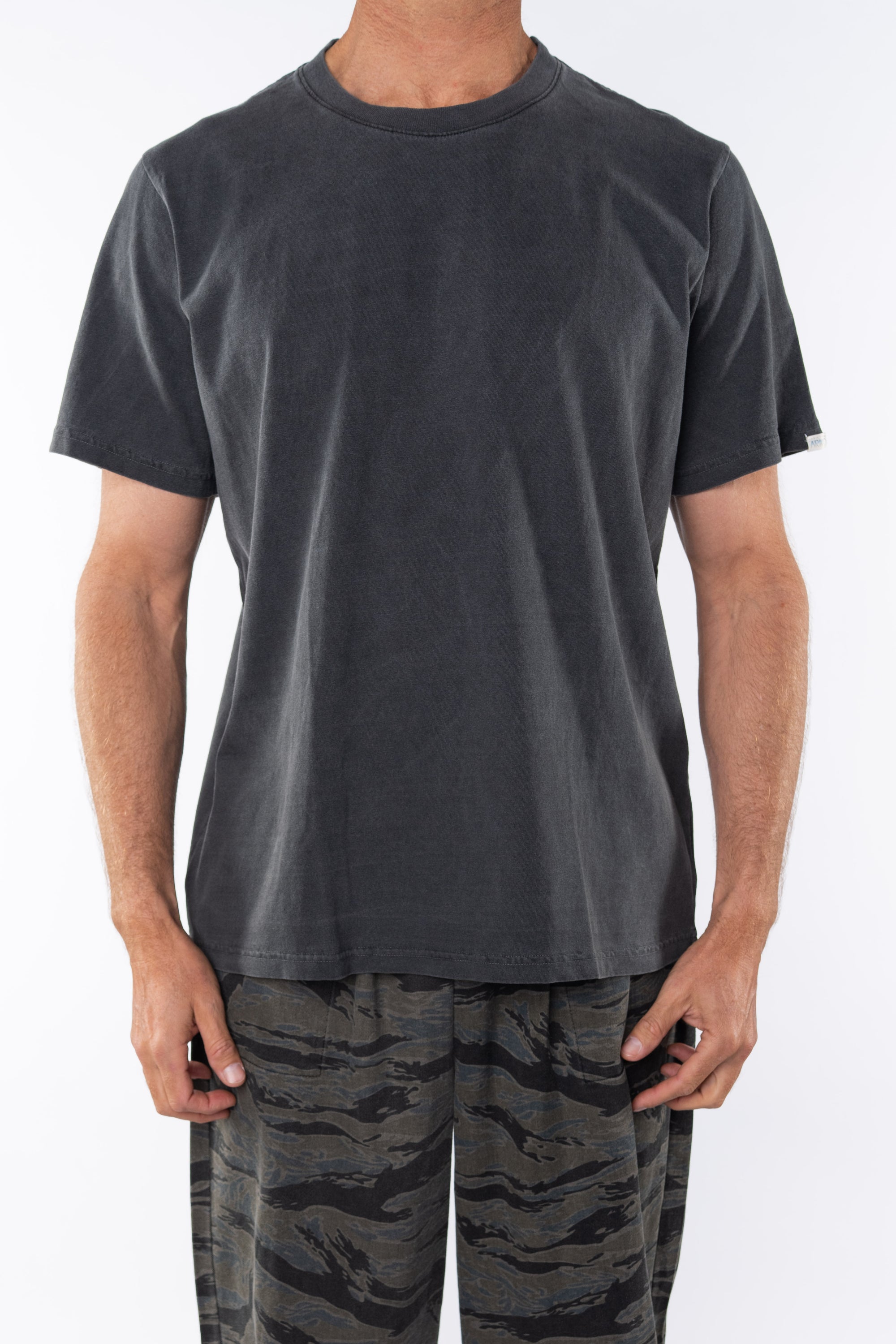 Man wearing a plain dark gray beach t-shirt and ocean tiger camo day pants on a white background