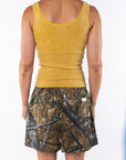 Back shot of a woman wearing a Scallop Tank in Sunrise Yellow with Real Tree Camo day shorts. 