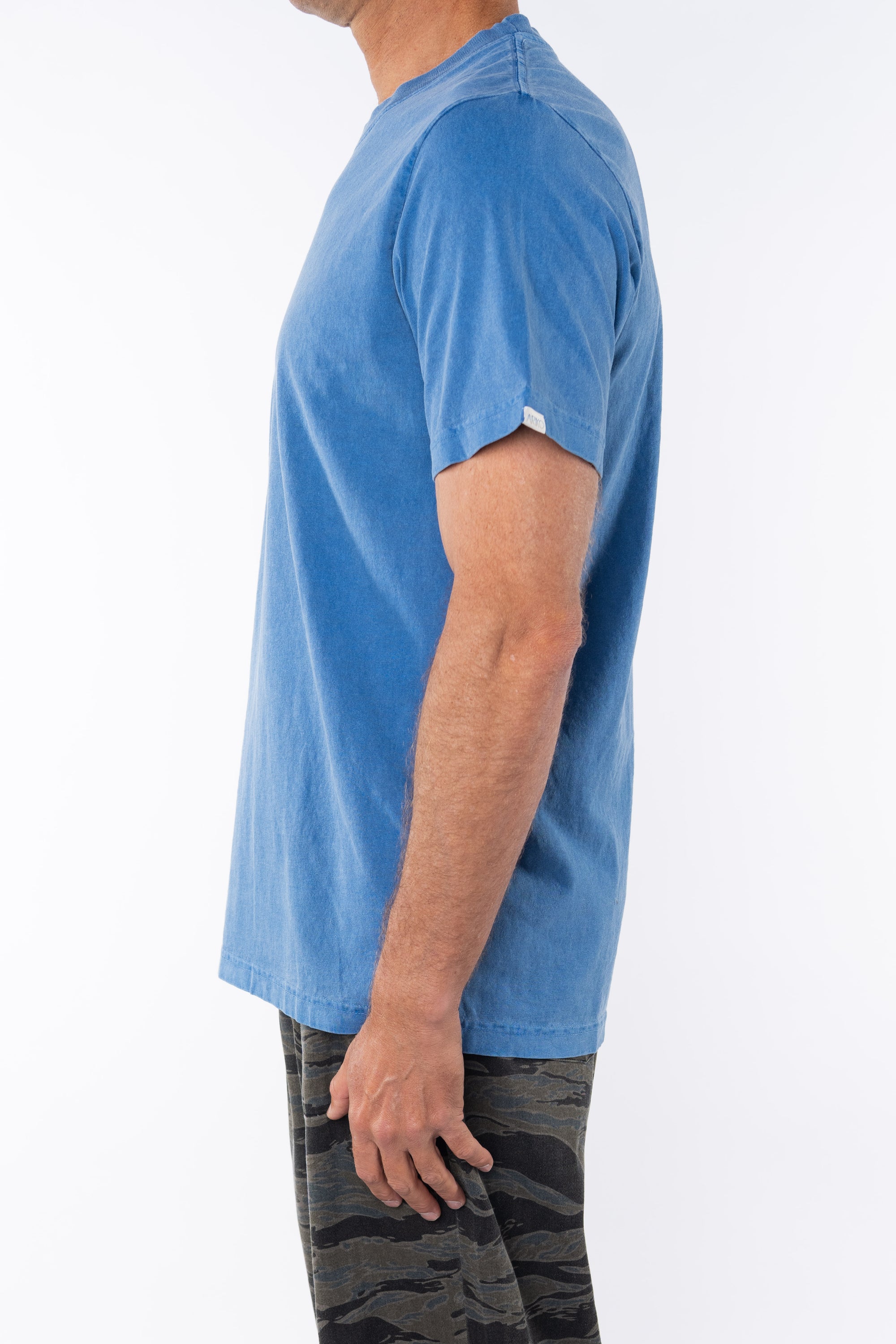 Side view of a man wearing a blue beach t-shirt with ocean tiger camo day pants on a white background 