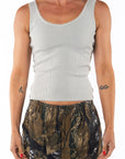 Woman wearing slight v-neck tank in cream and real tree camo pants on a white background