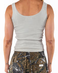 Back view of a woman wearing a beige ribbed tank top and real tree camouflage day pants on a white background