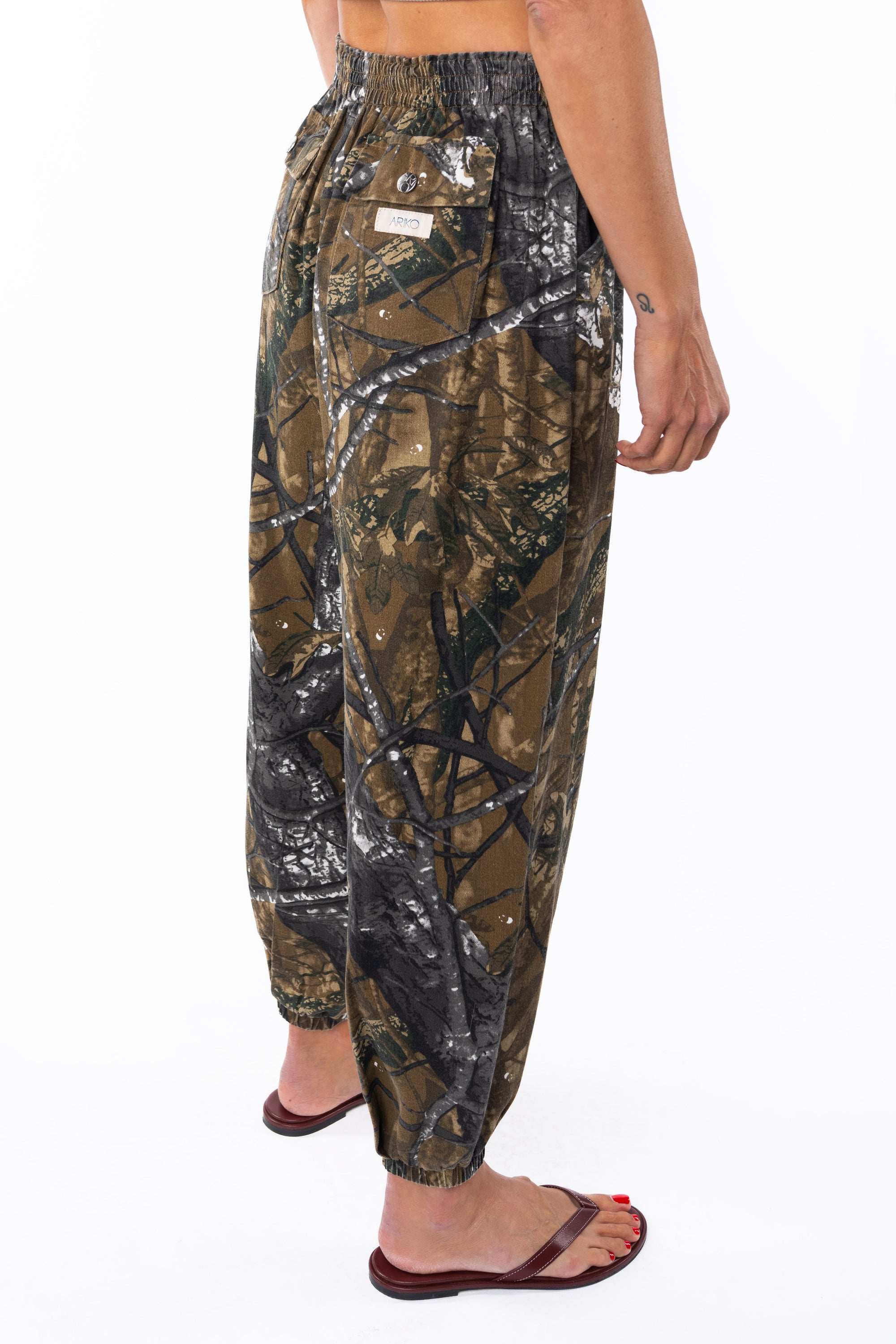 Side back view of a woman wearing real tree camo day pants on a white background