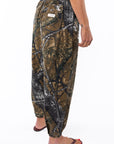 Side back view of a woman wearing real tree camo day pants on a white background