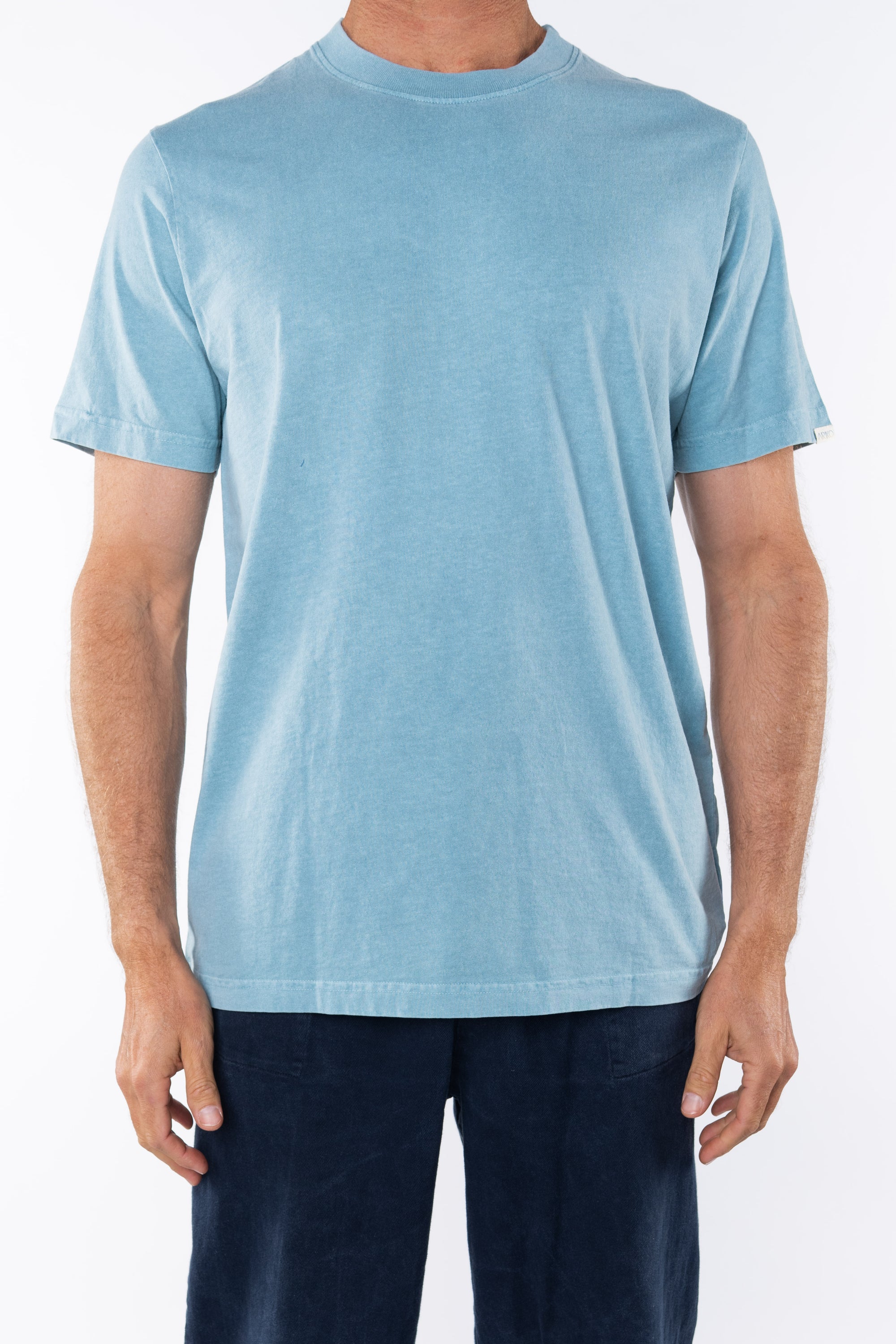 Man wearing light blue ocean beach t-shirt and navy day pants on white background